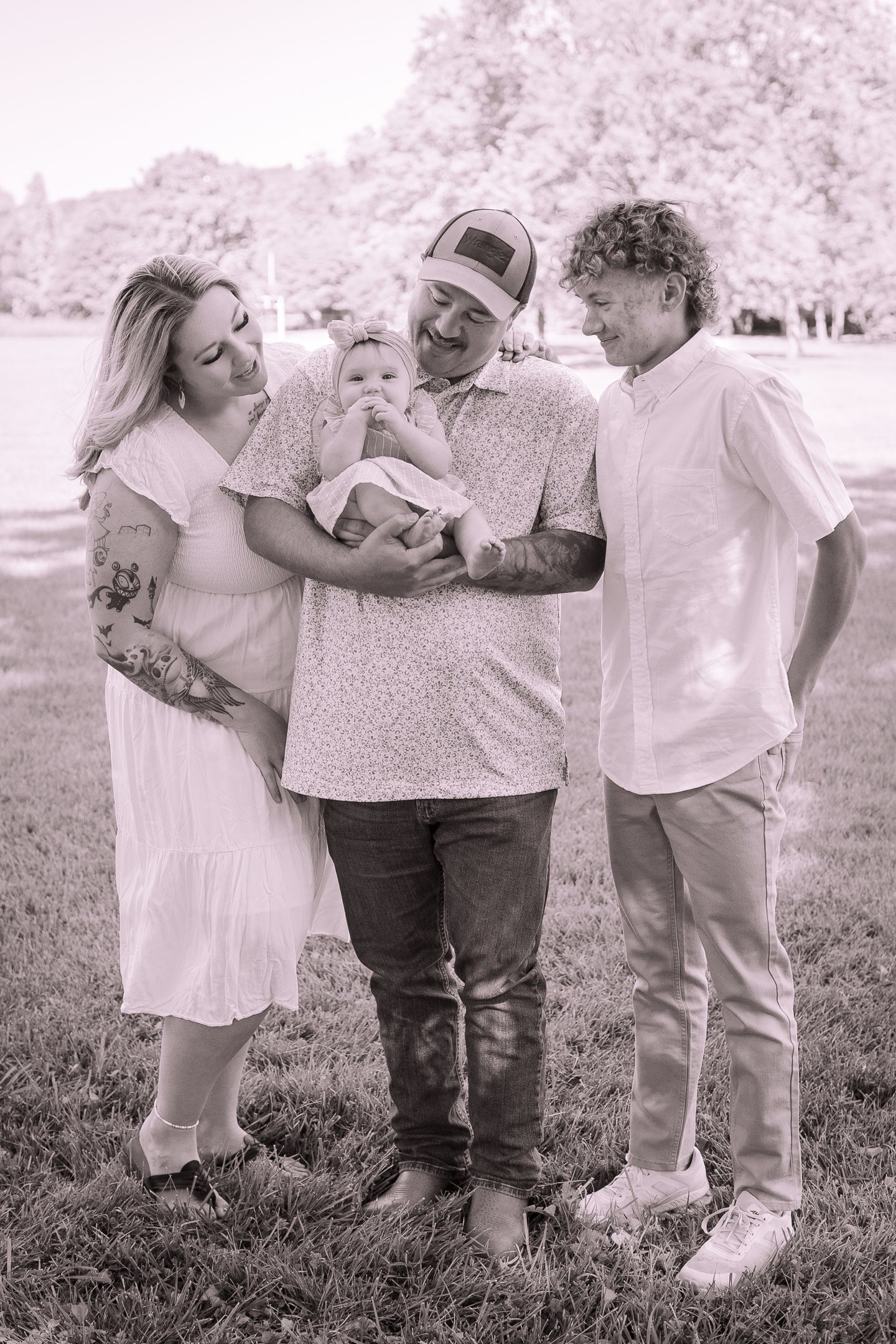 Family group shares tender moments together on grassy field in black and white photography.