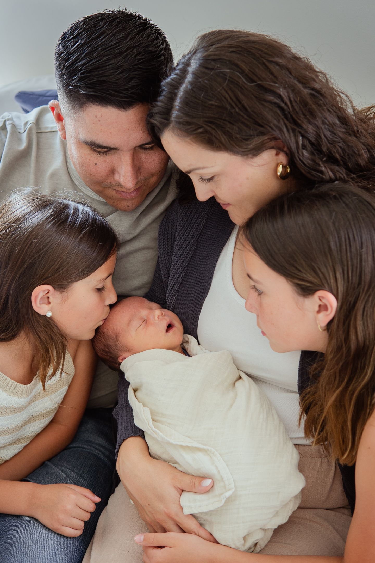 A family gathers close together on a couch for an intimate moment with their newborn.