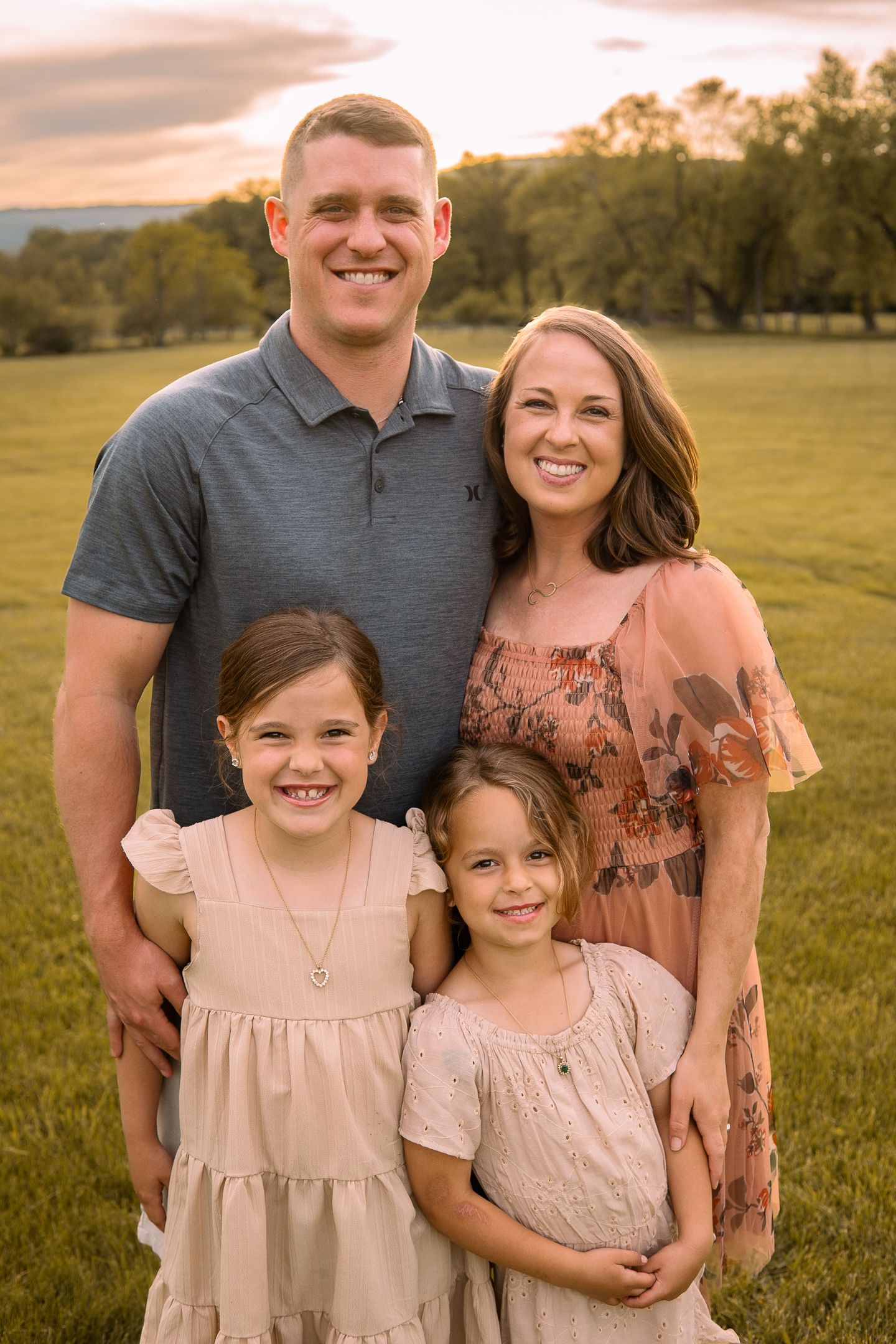 A family of four poses together outdoors in coordinating pink outfits during golden hour at sunset.