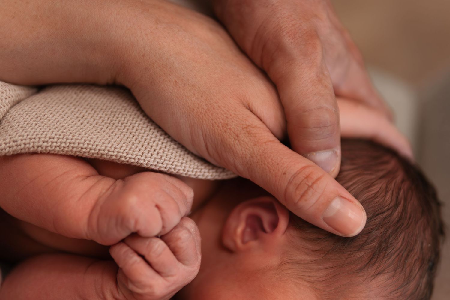 Close-up of gentle hands cradling newborn baby's tiny fingers.
