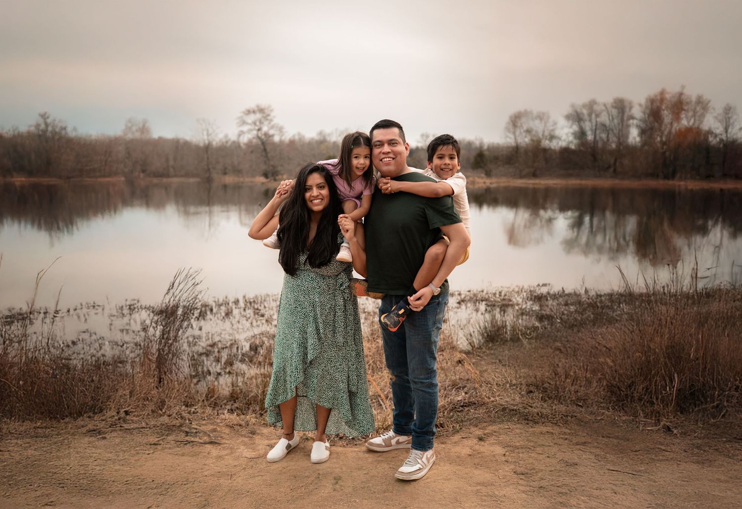A happy family poses together for a portrait by a serene lake at sunset.