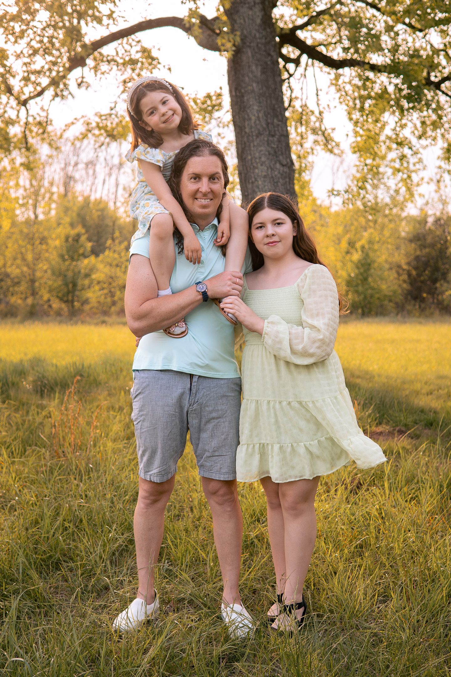 Family portrait in a sunlit autumn field with golden foliage and trees in the background.