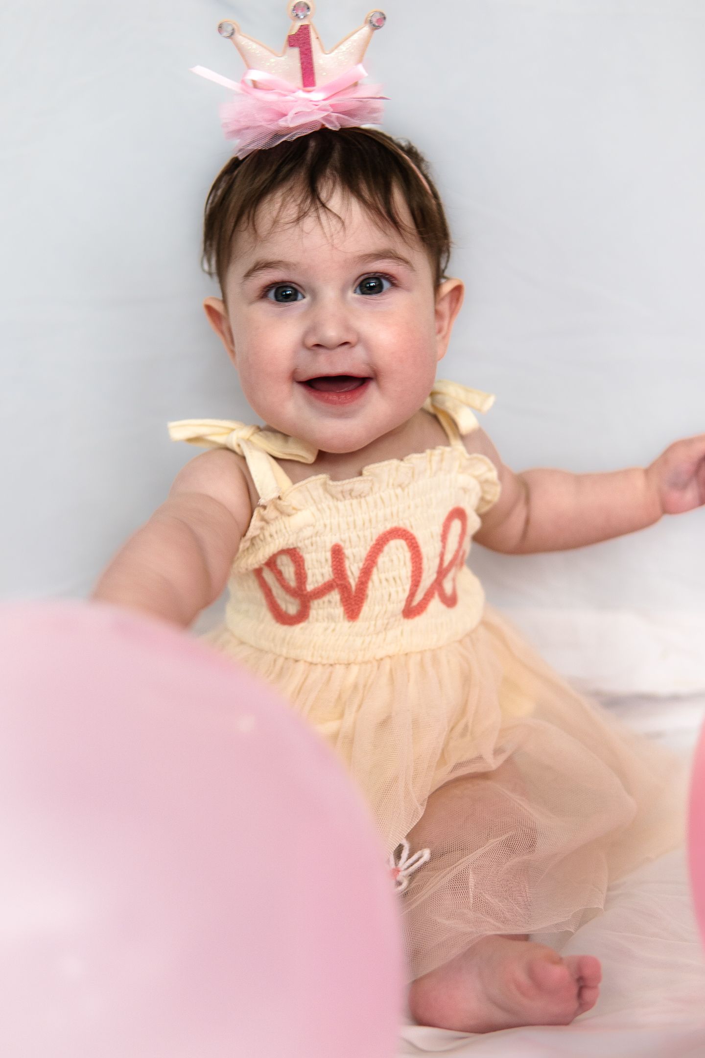 Baby wearing peach tulle dress with pink bow sitting against white background.