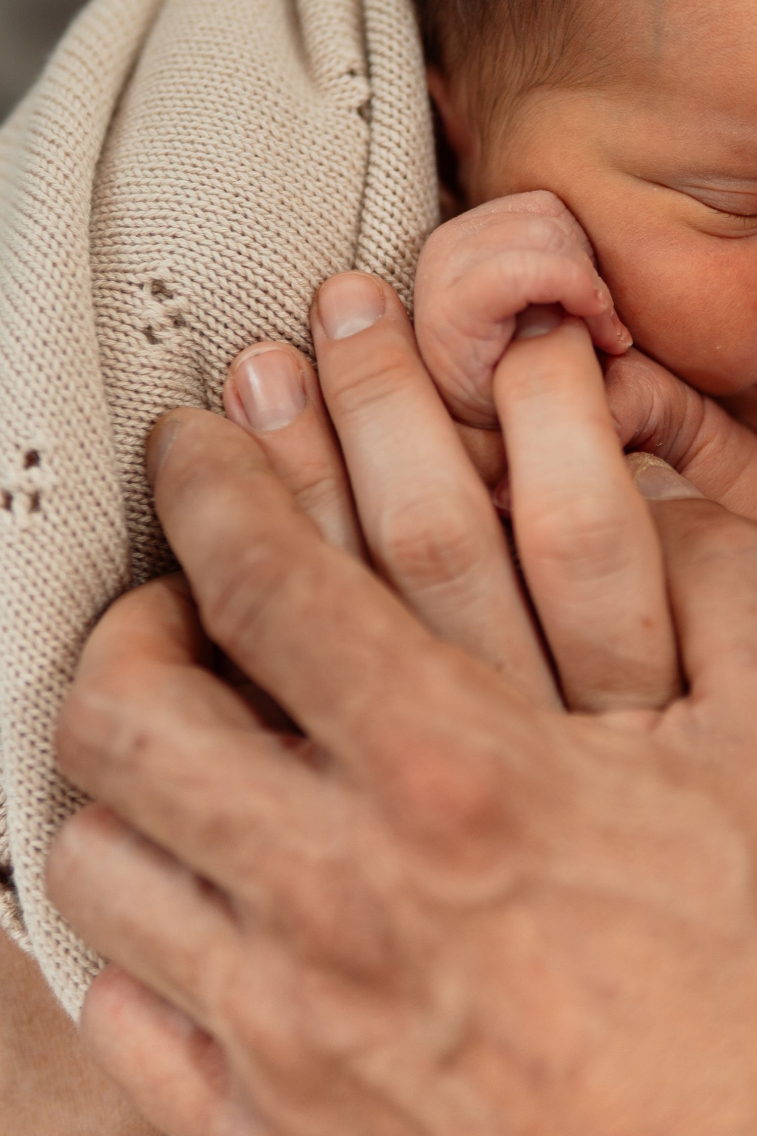 Intimate close-up of parent's hand gently touching newborn wrapped in knit blanket.