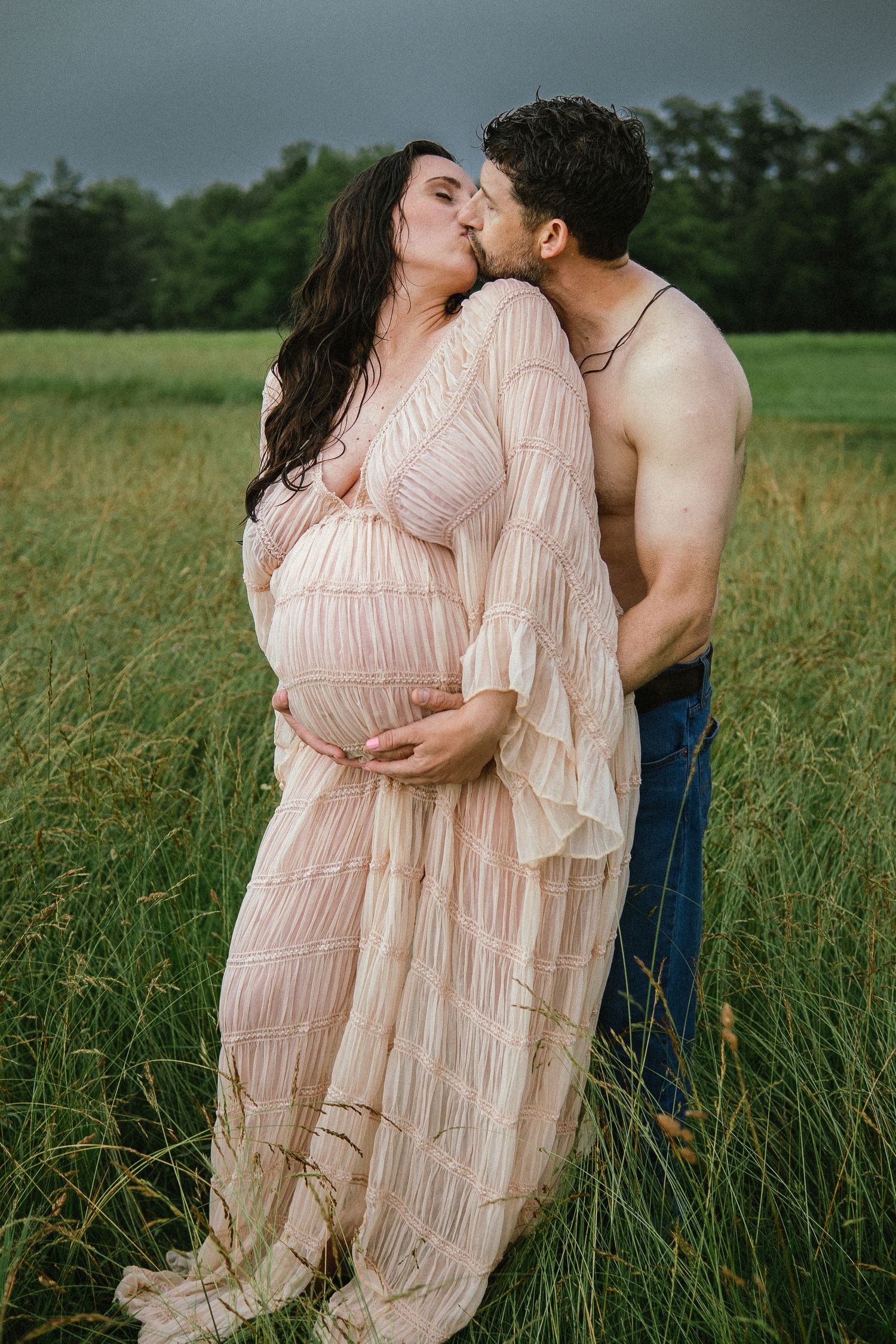 Intimate outdoor photoshoot of couple in field with woman in flowing pink dress and man in denim.