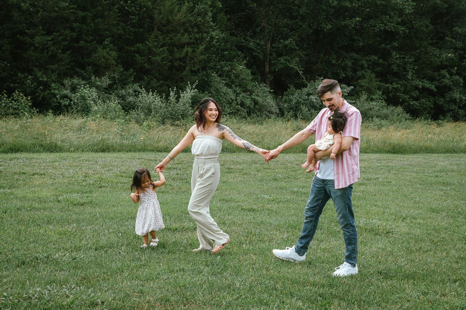 A family holds hands while walking together across a sunny green field on a summer day.
