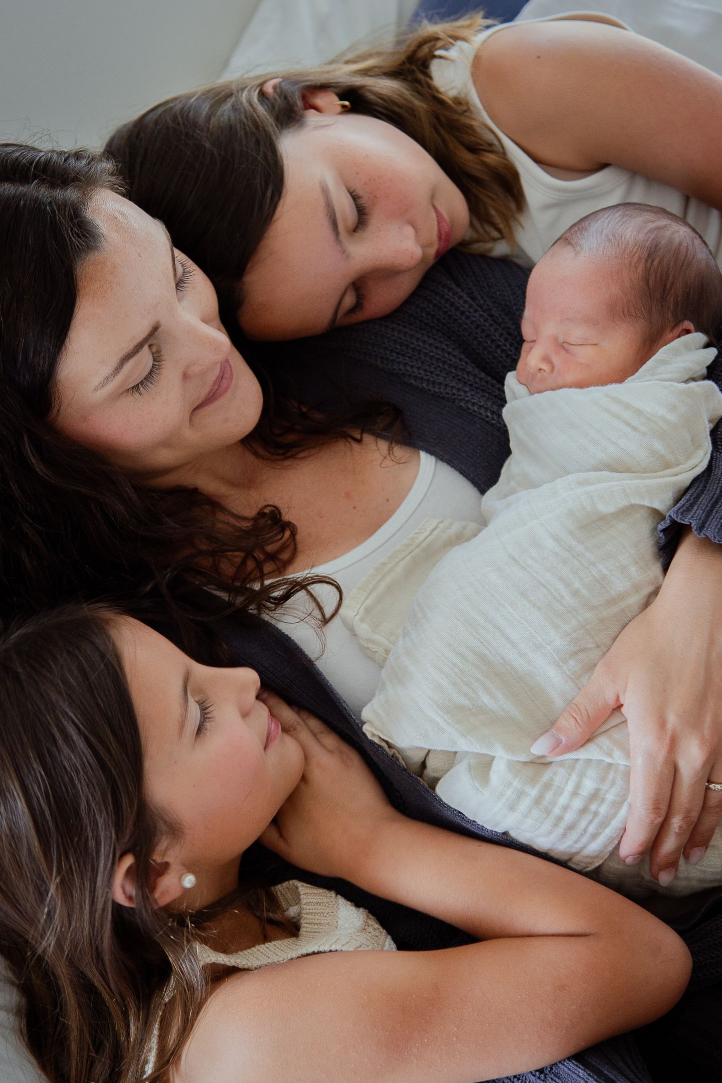 Intimate family cuddle with newborn baby wrapped in white swaddle.