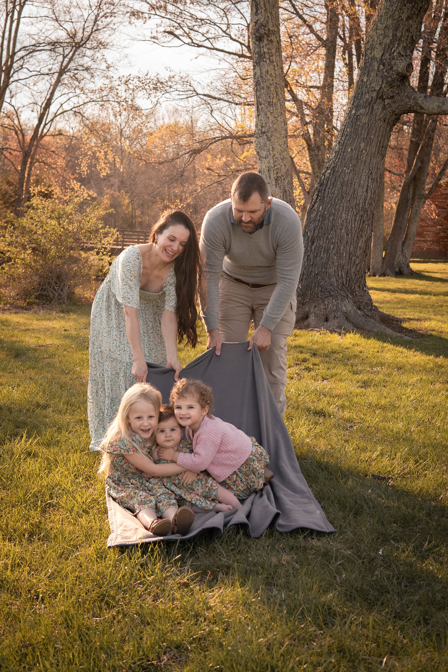 A tender family moment captured in warm autumn sunlight with trees and grass in the background.