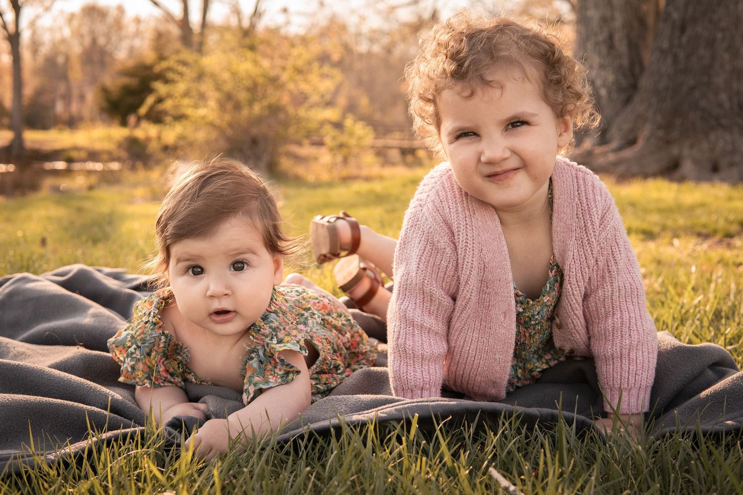 Two children laying on a blanket outdoors during autumn with sunlit trees in the background in Haymarket, Virginia.