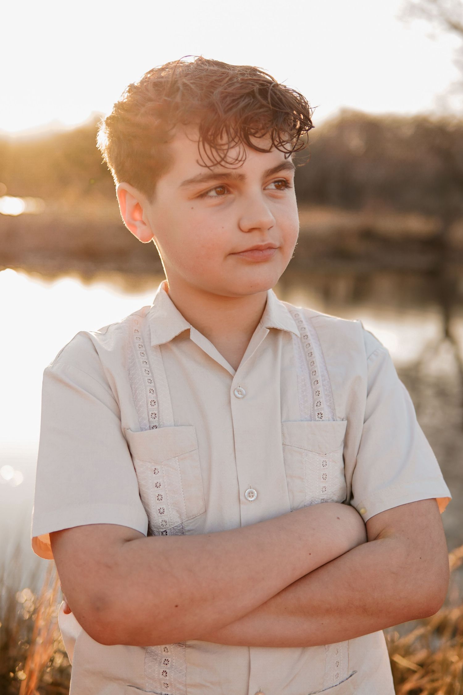 A person in a white button-down shirt poses near a body of water at golden hour during sunset.
