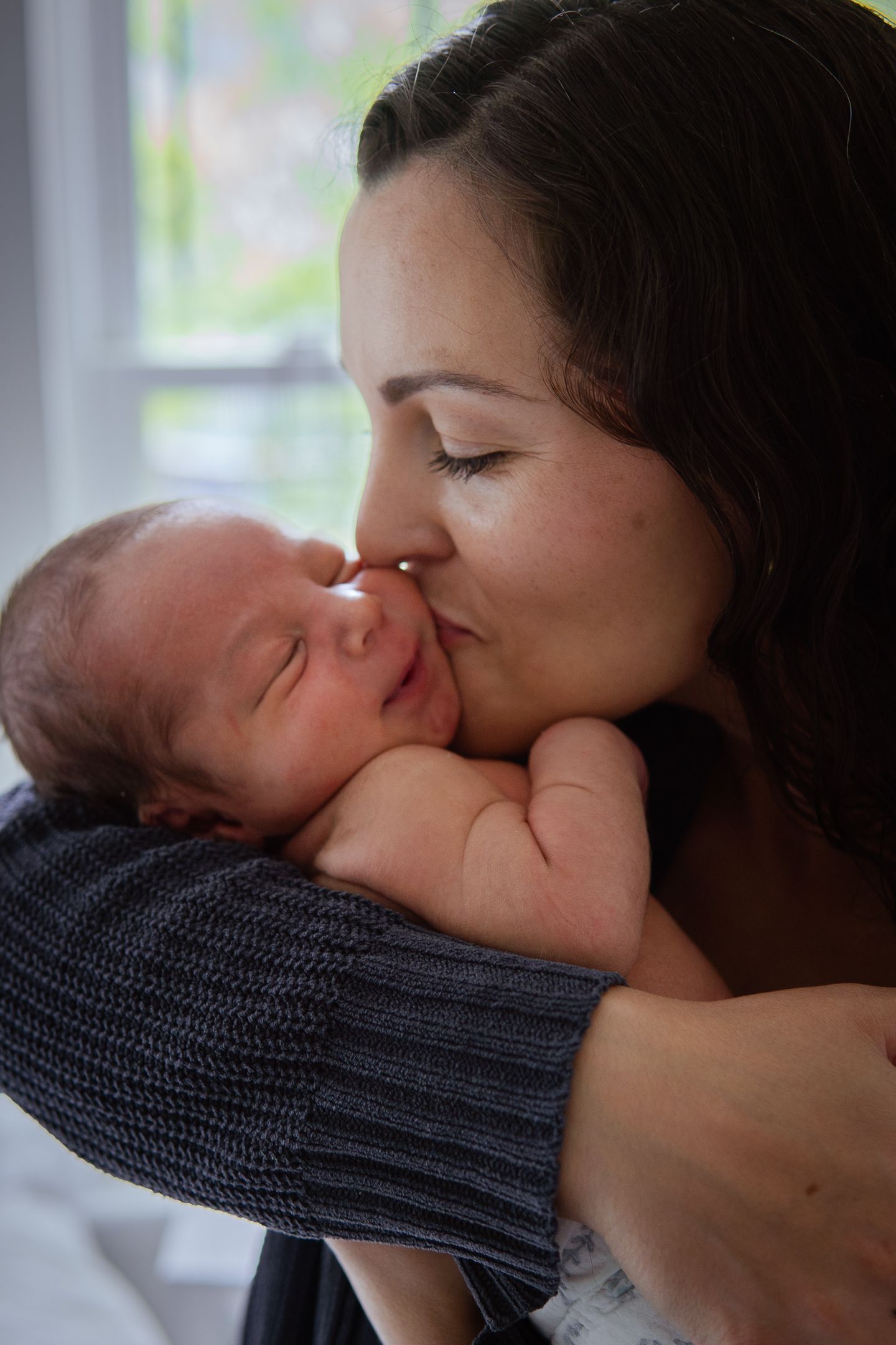 Tender moment between parent and newborn baby swaddled in knit blanket.