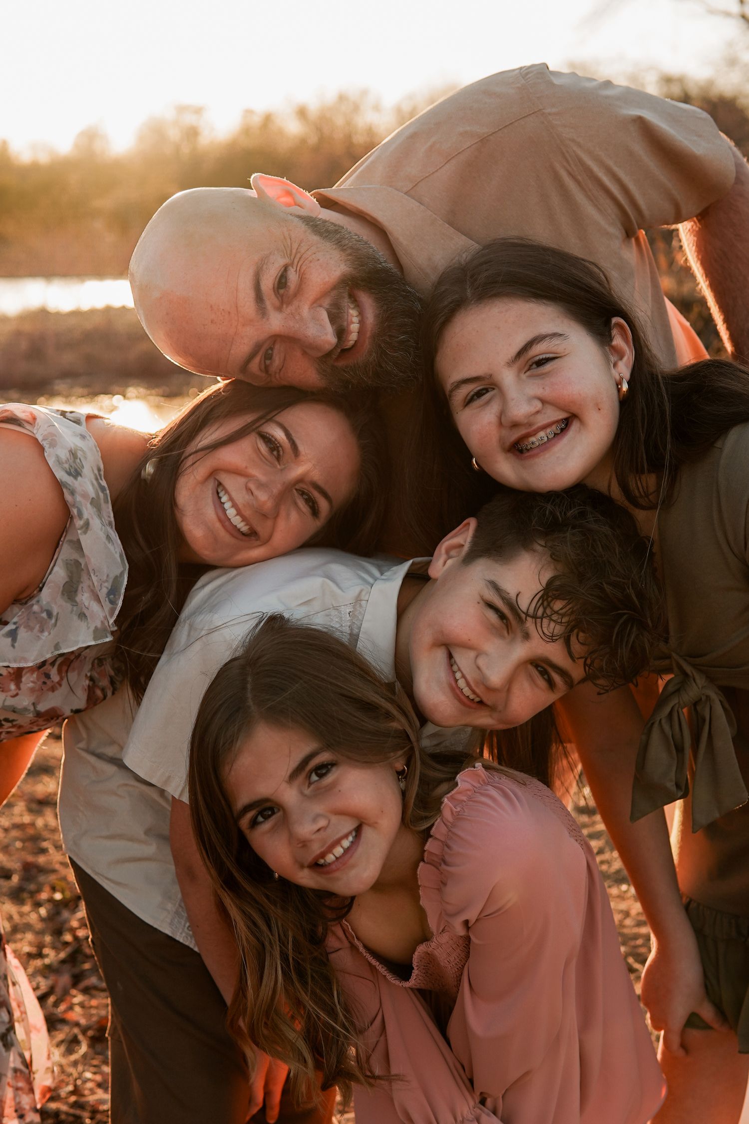 A group of people embrace and laugh together during a warm golden hour photo session outdoors.