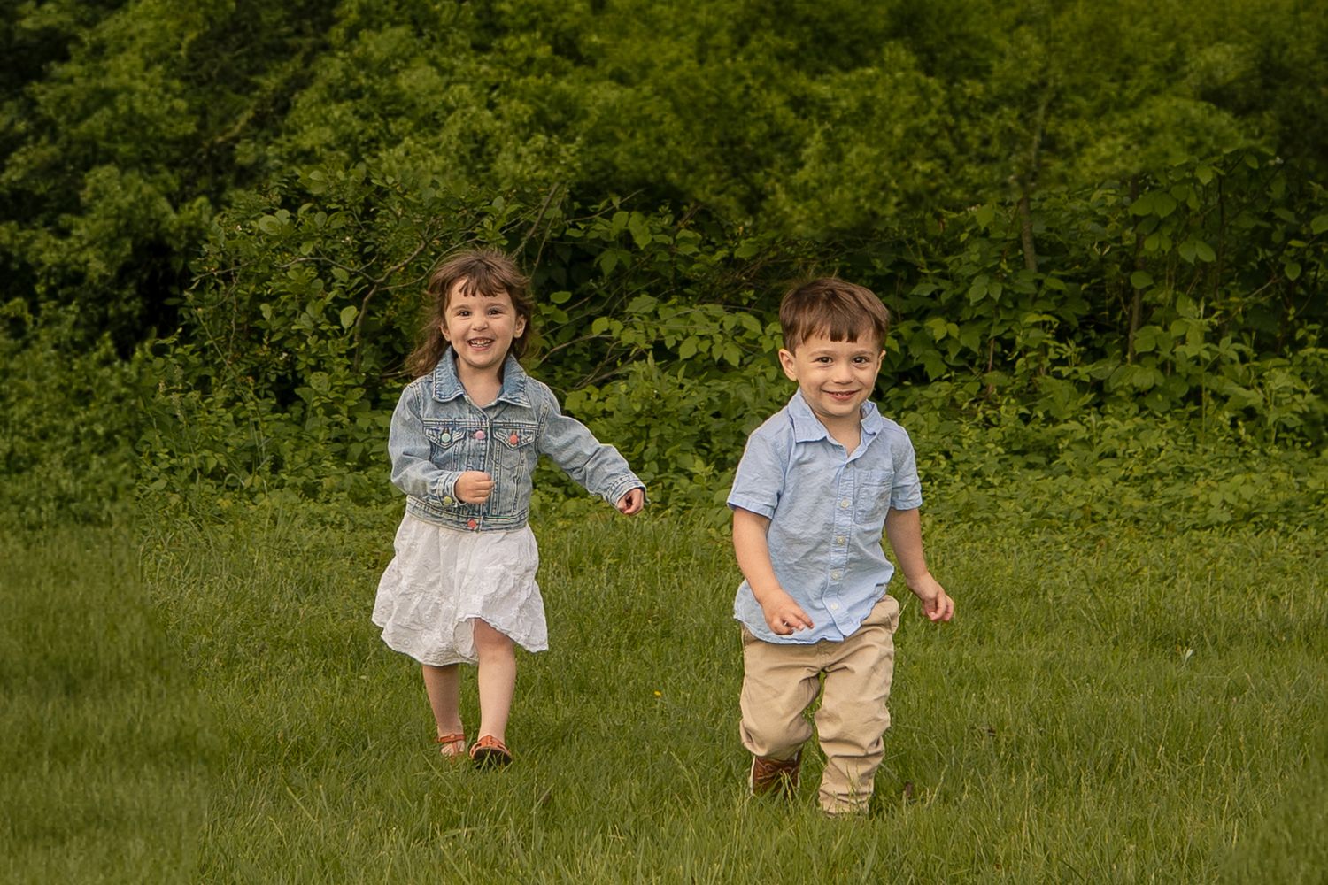Two children run and play together in a lush green field on a sunny summer day.
