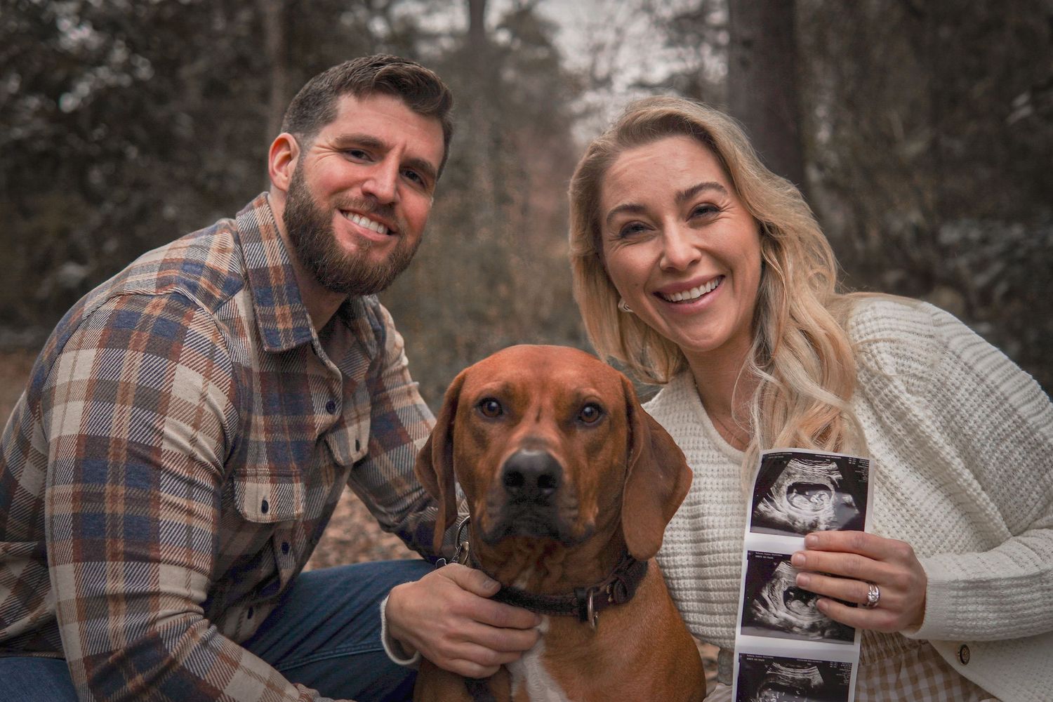 A couple sits outdoors with their brown dog while holding an ultrasound photo in a heartwarming pregnancy announcement.