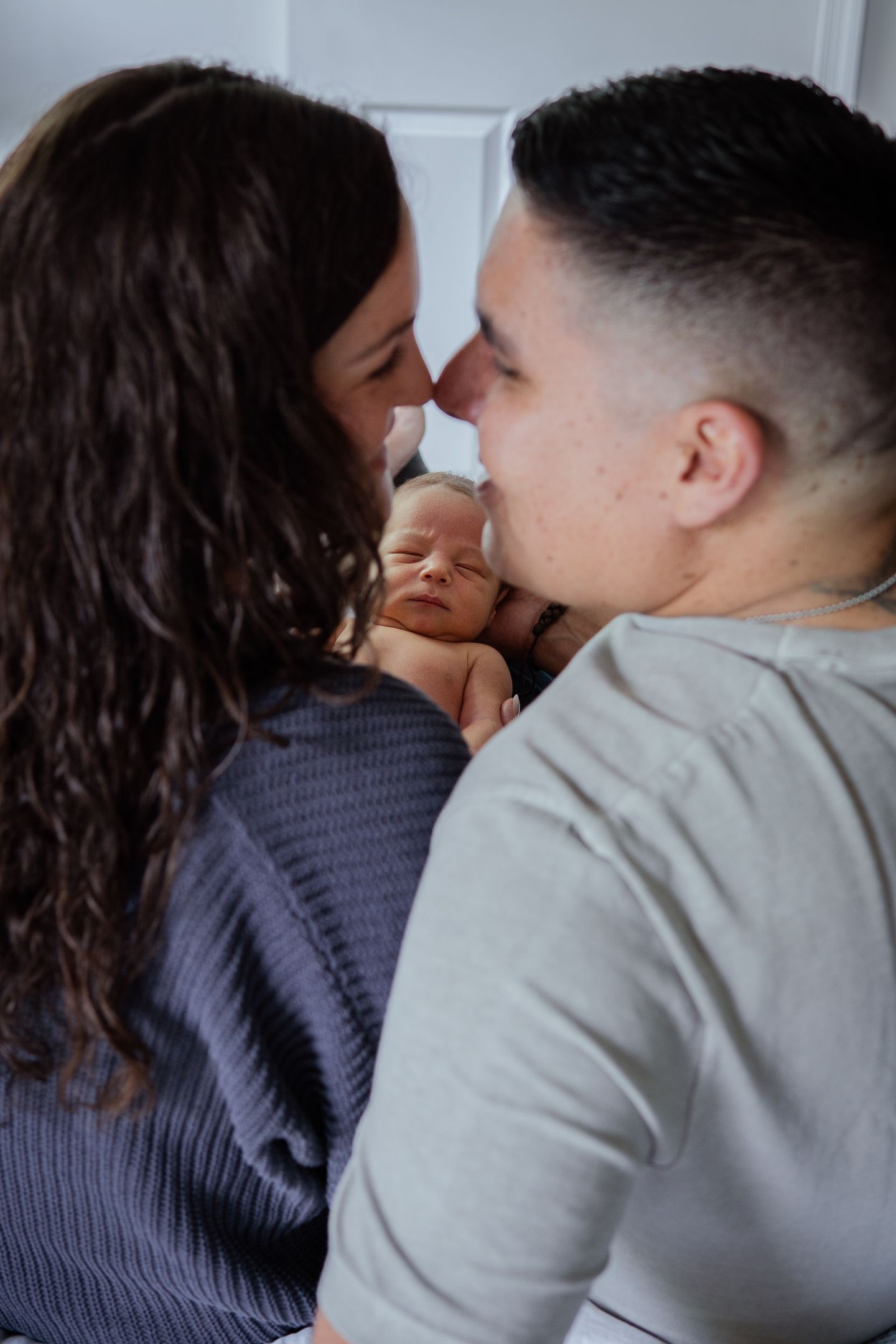 Parents lovingly embrace their newborn baby between them during an intimate photo session.