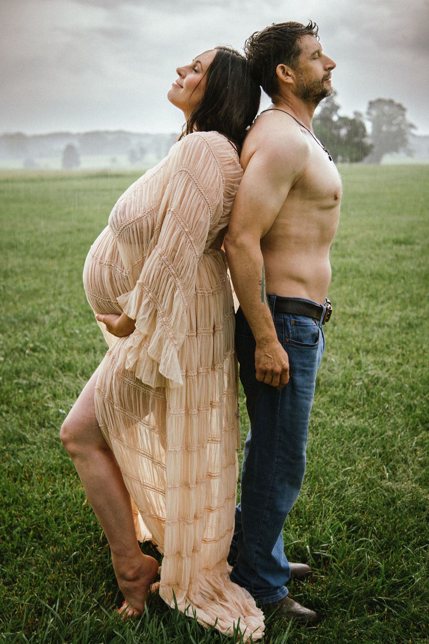 A couple stands back-to-back in a dreamy outdoor maternity photo on a foggy morning.