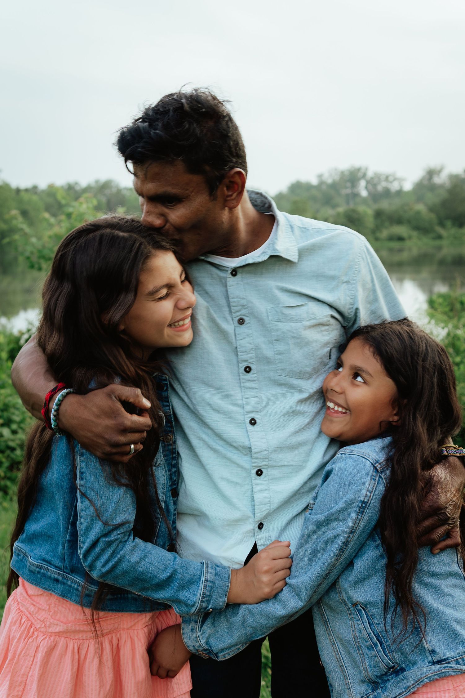 A loving family shares an intimate embrace outdoors while wearing casual denim and smiling warmly together.