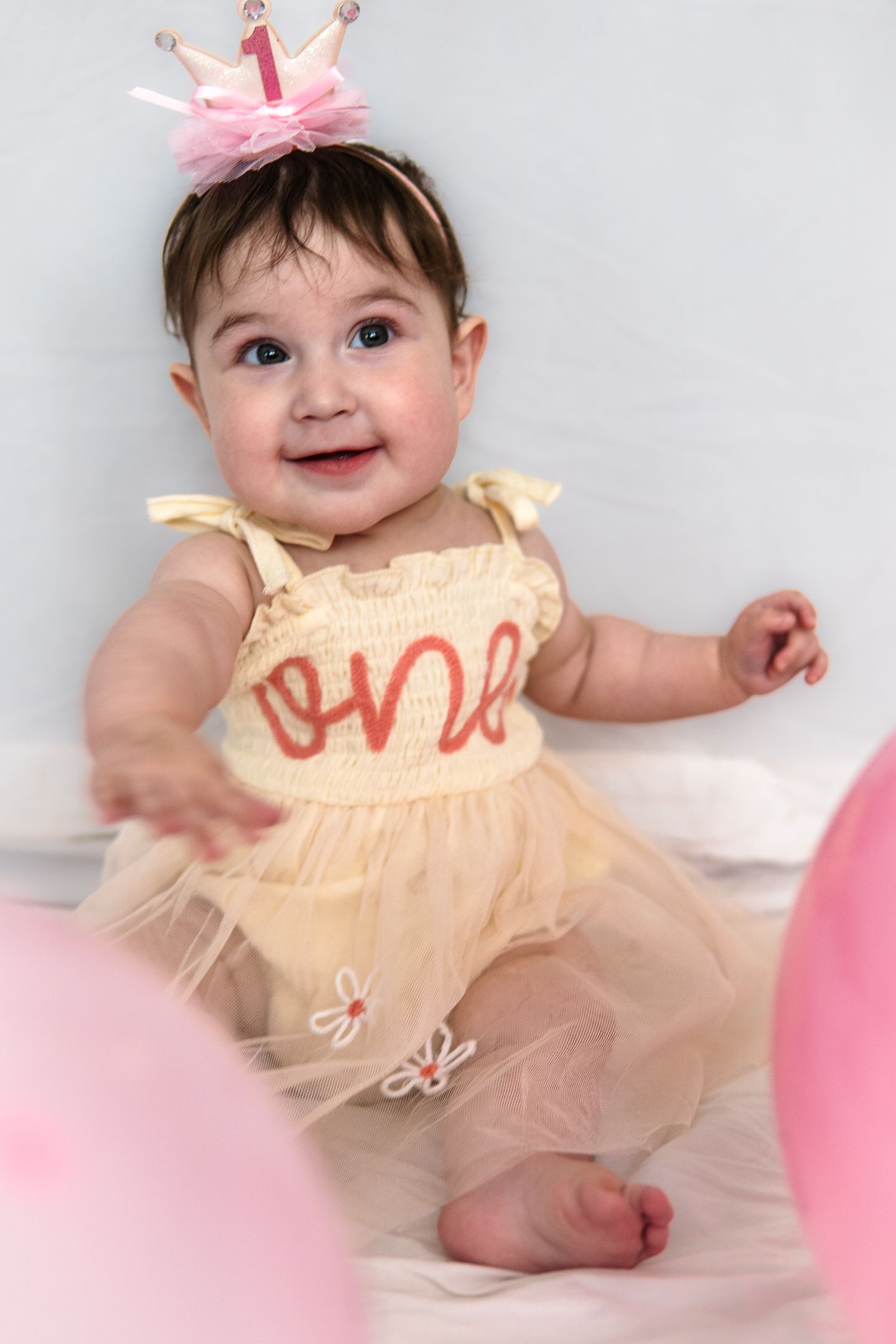 First birthday celebration setup with a pale yellow tulle dress and pink crown against white backdrop.