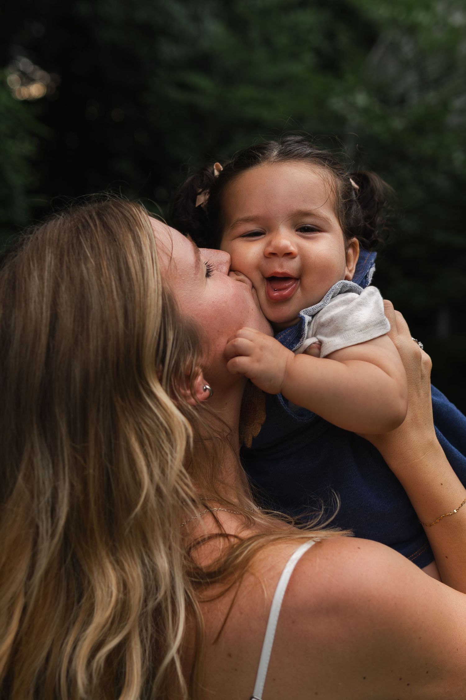 A joyful parenting moment captured as a baby laughs while being held up in the sunshine outdoors.