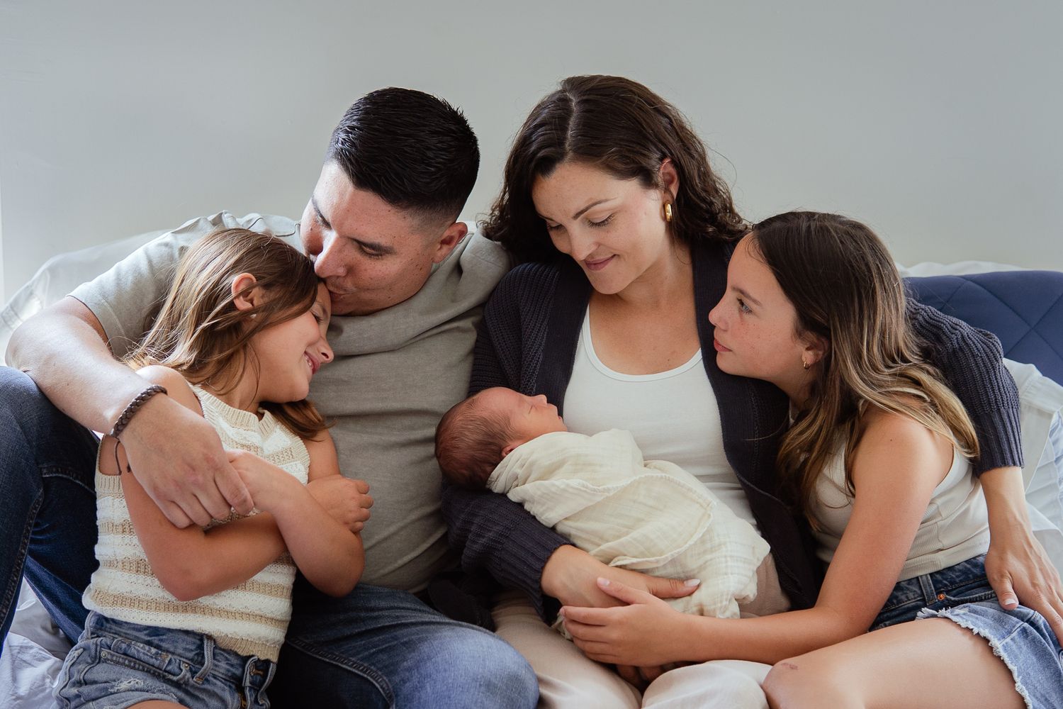 Family lying together showing affection and bonding on light background.