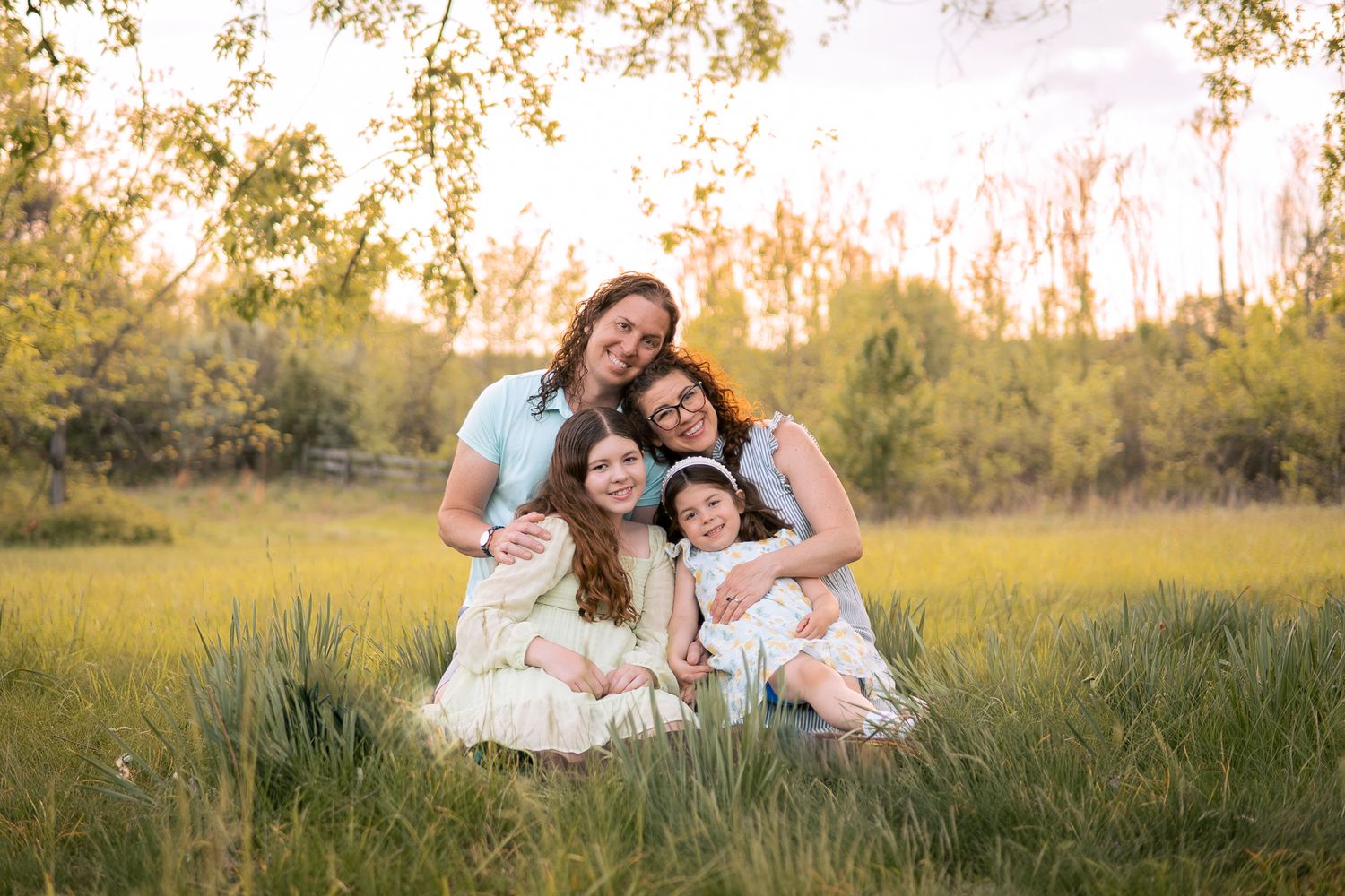 A family sits together in a golden field during sunset as they share joyful laughter in matching white outfits.