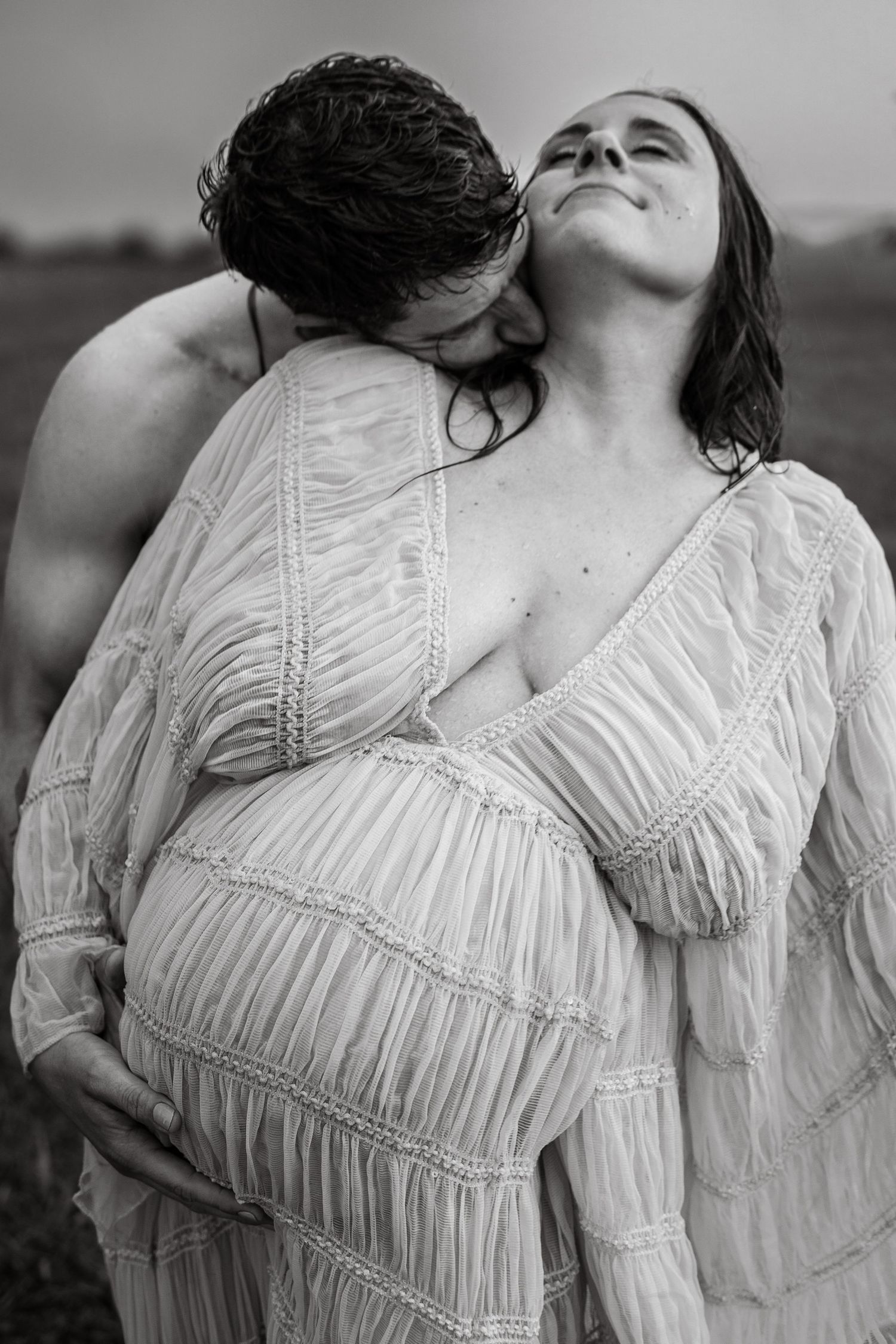 An intimate black and white maternity photo of a couple embracing in a field.