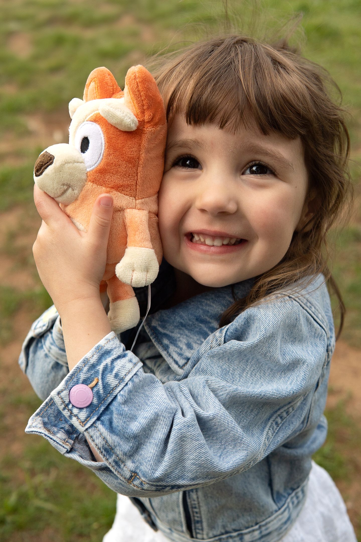 Smiling child in denim jacket holding orange plush toy animal outdoors.