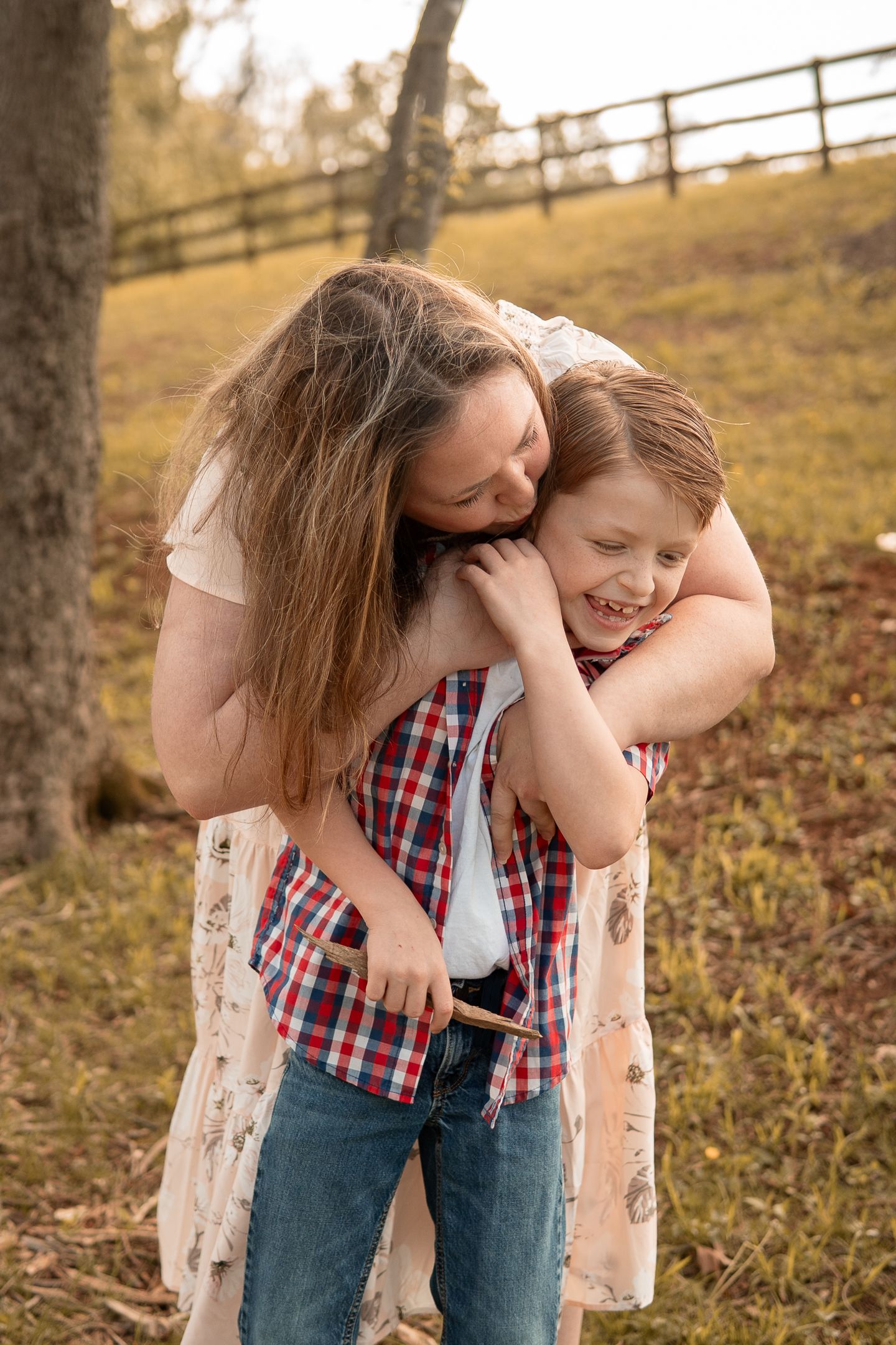 A sweet hug and playful moment between two people outdoors in autumn with a rustic fence in the background.