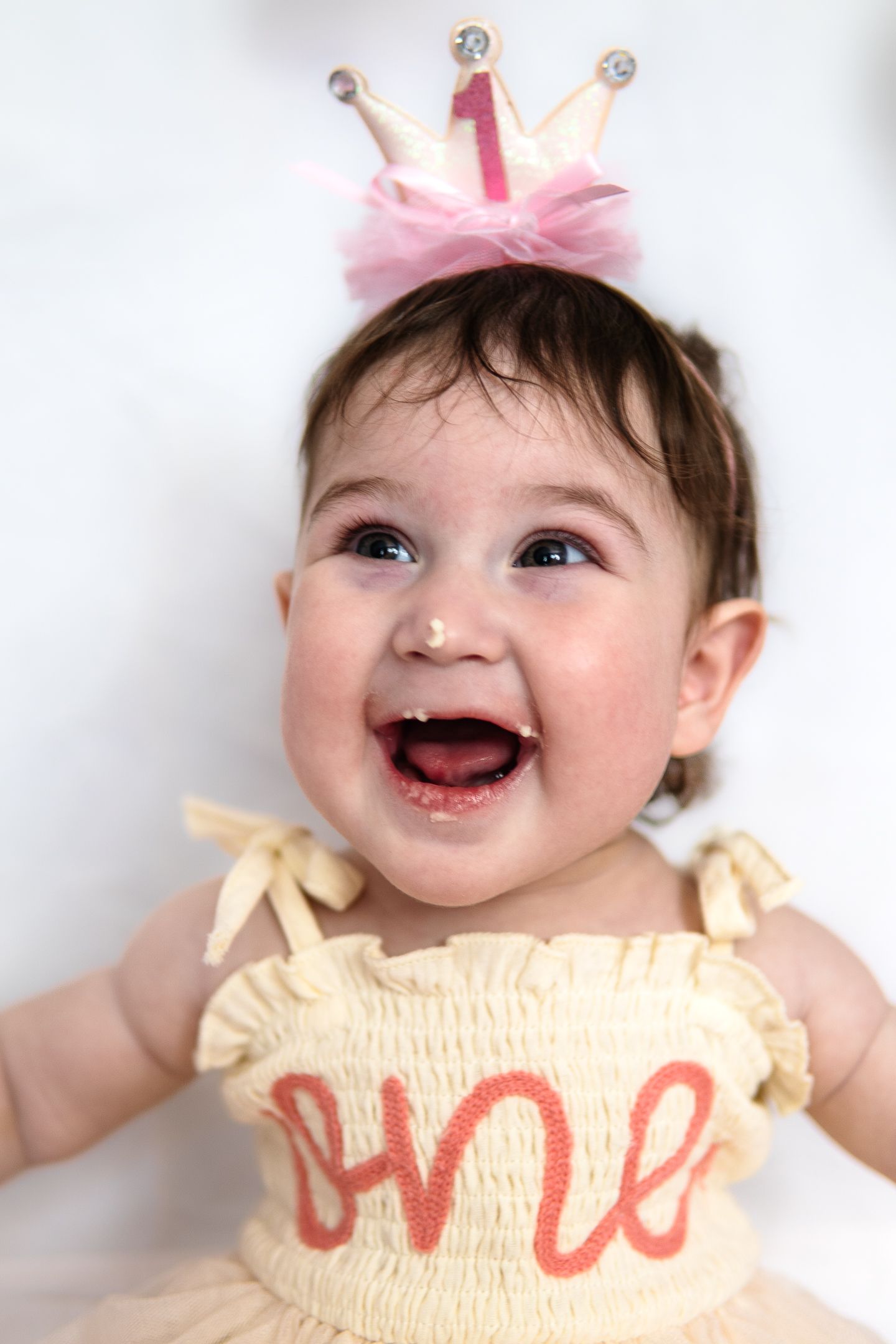 A cute baby wearing a cream-colored outfit smiles joyfully against a white background.