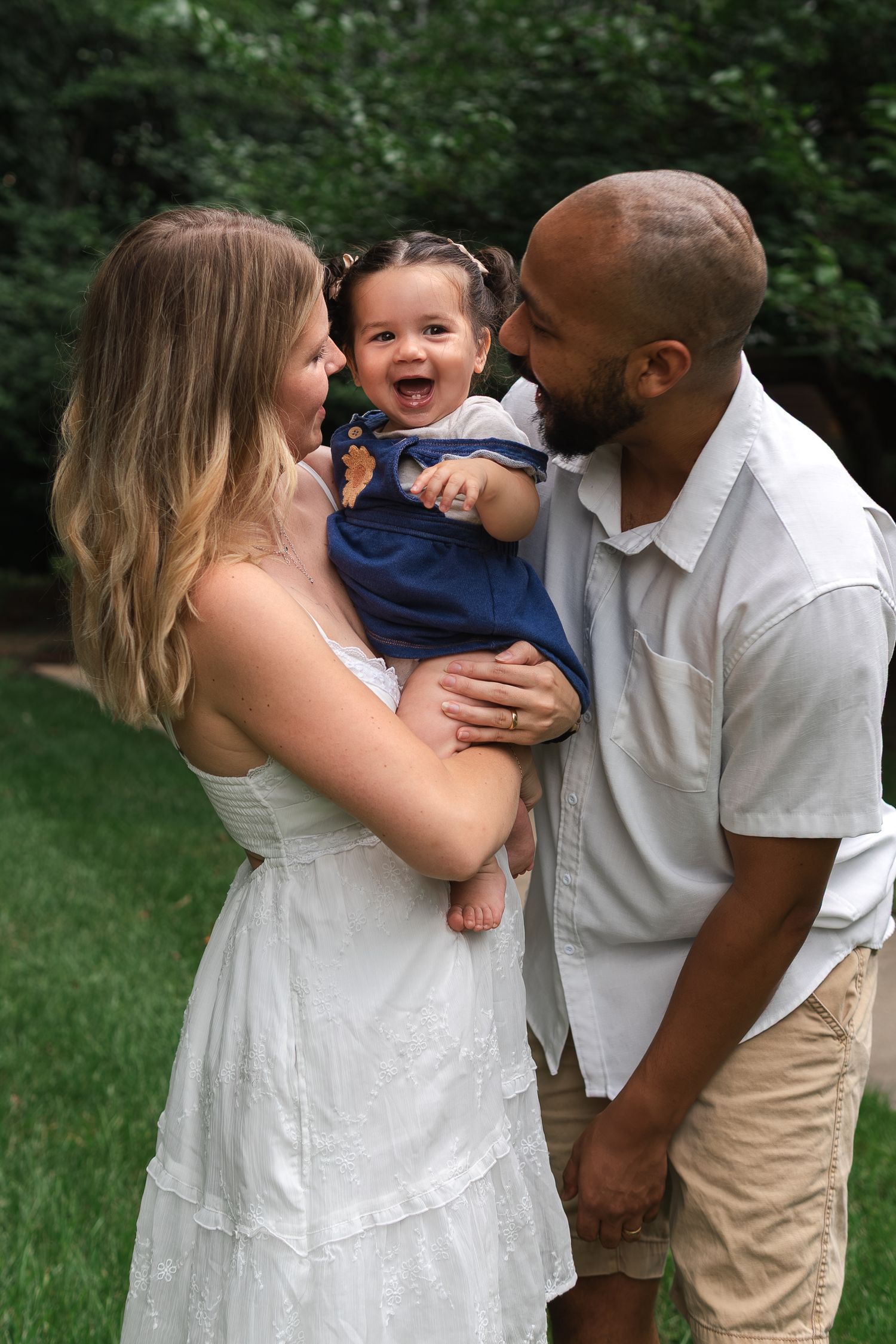 A joyful family shares laughs and embraces while taking candid photos together outdoors in a grassy area.