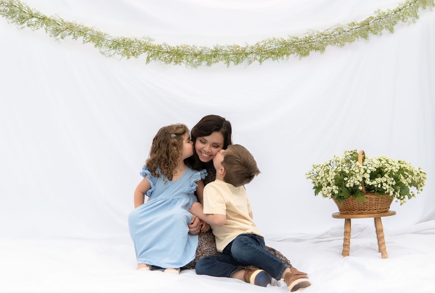 Sweet moment of affection shared between family members against white backdrop with floral garland decor.