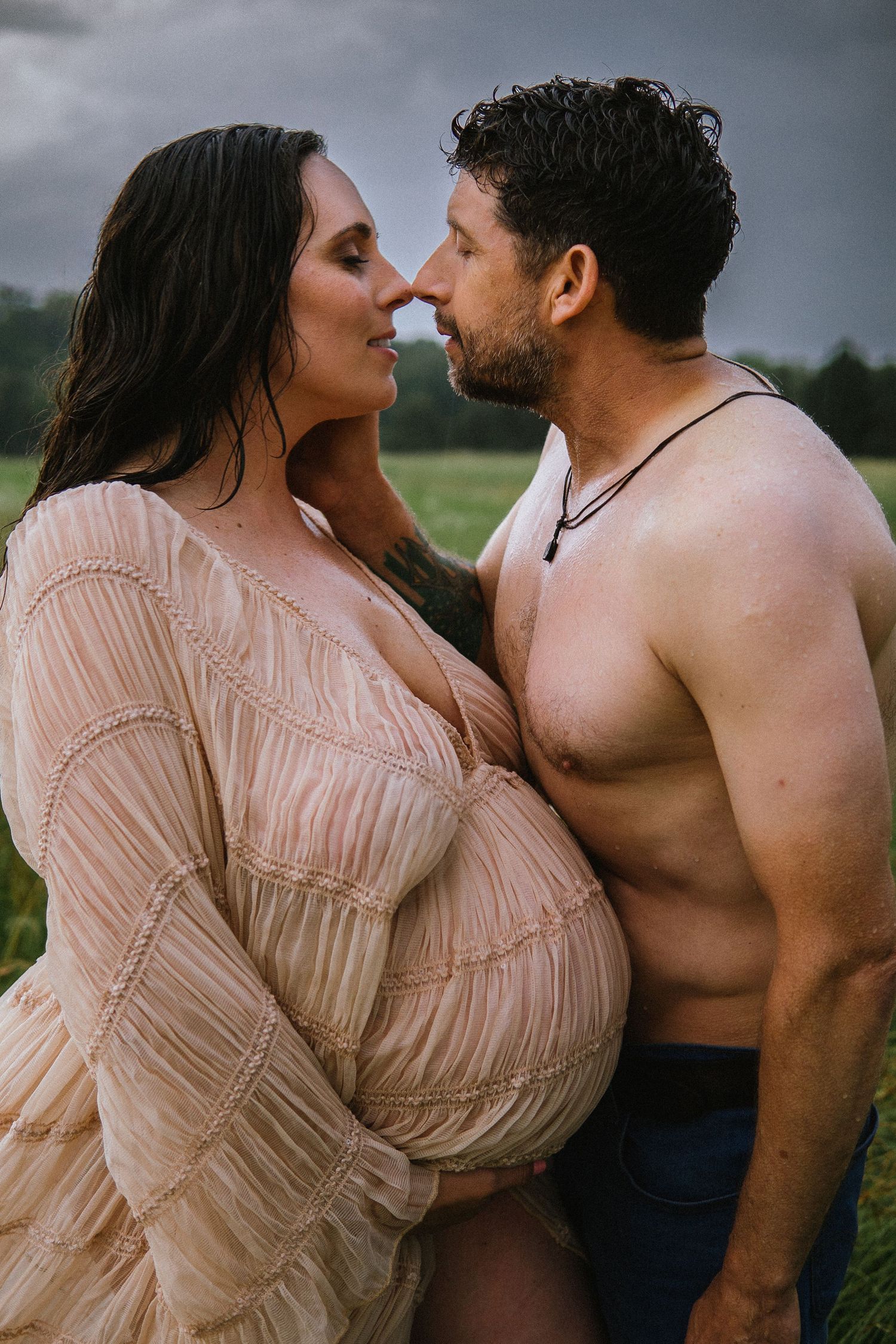 A romantic maternity photoshoot outdoors with couple in soft lighting wearing blush tones against moody sky.