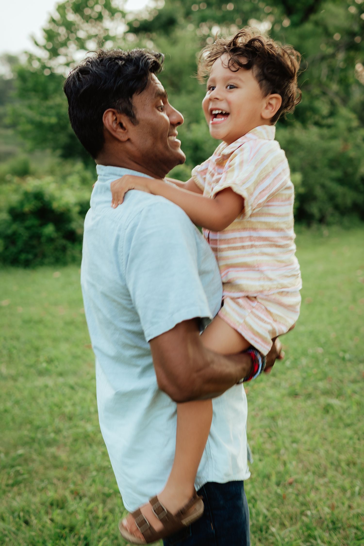 Parent and child sharing an enthusiastic laugh while playing outdoors in a grassy field.