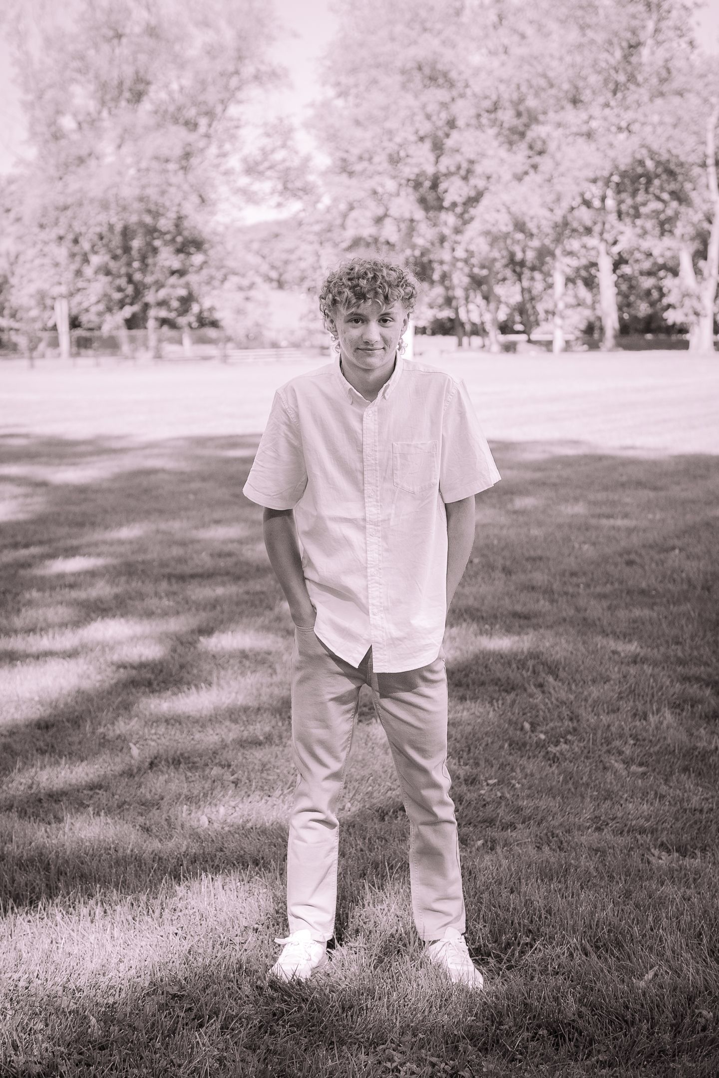 Black and white portrait of someone in a white button-down shirt standing on grass in natural lighting.