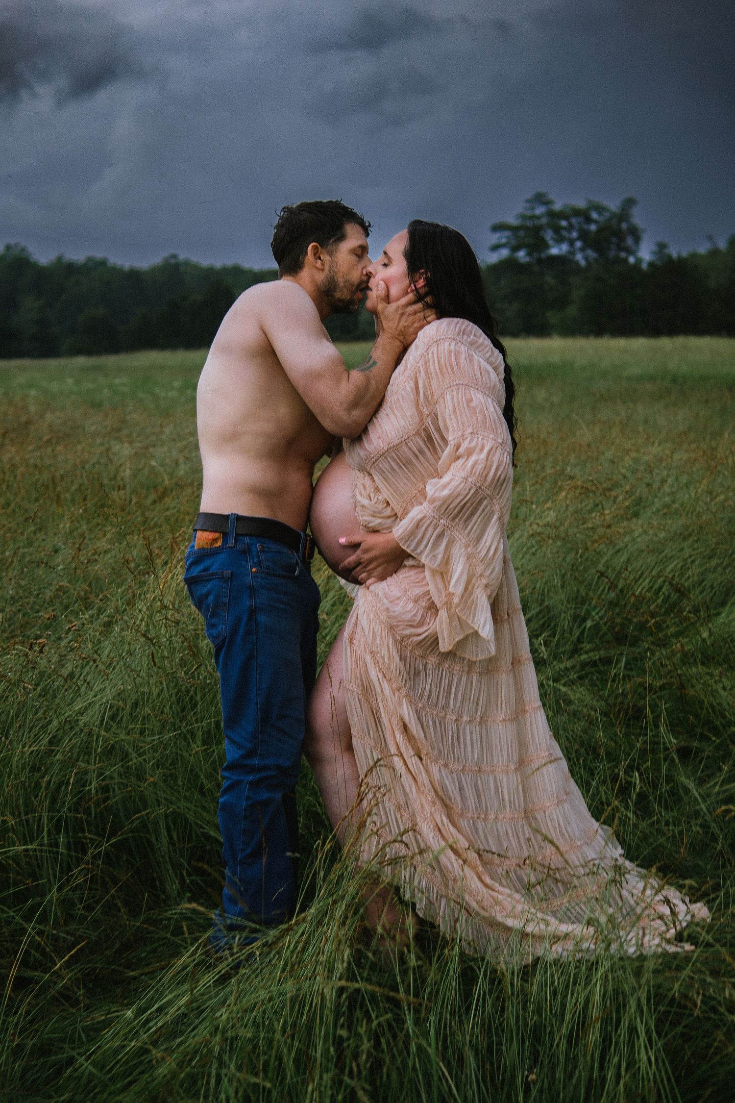 An intimate maternity portrait captures a tender moment between partners in a windswept field.
