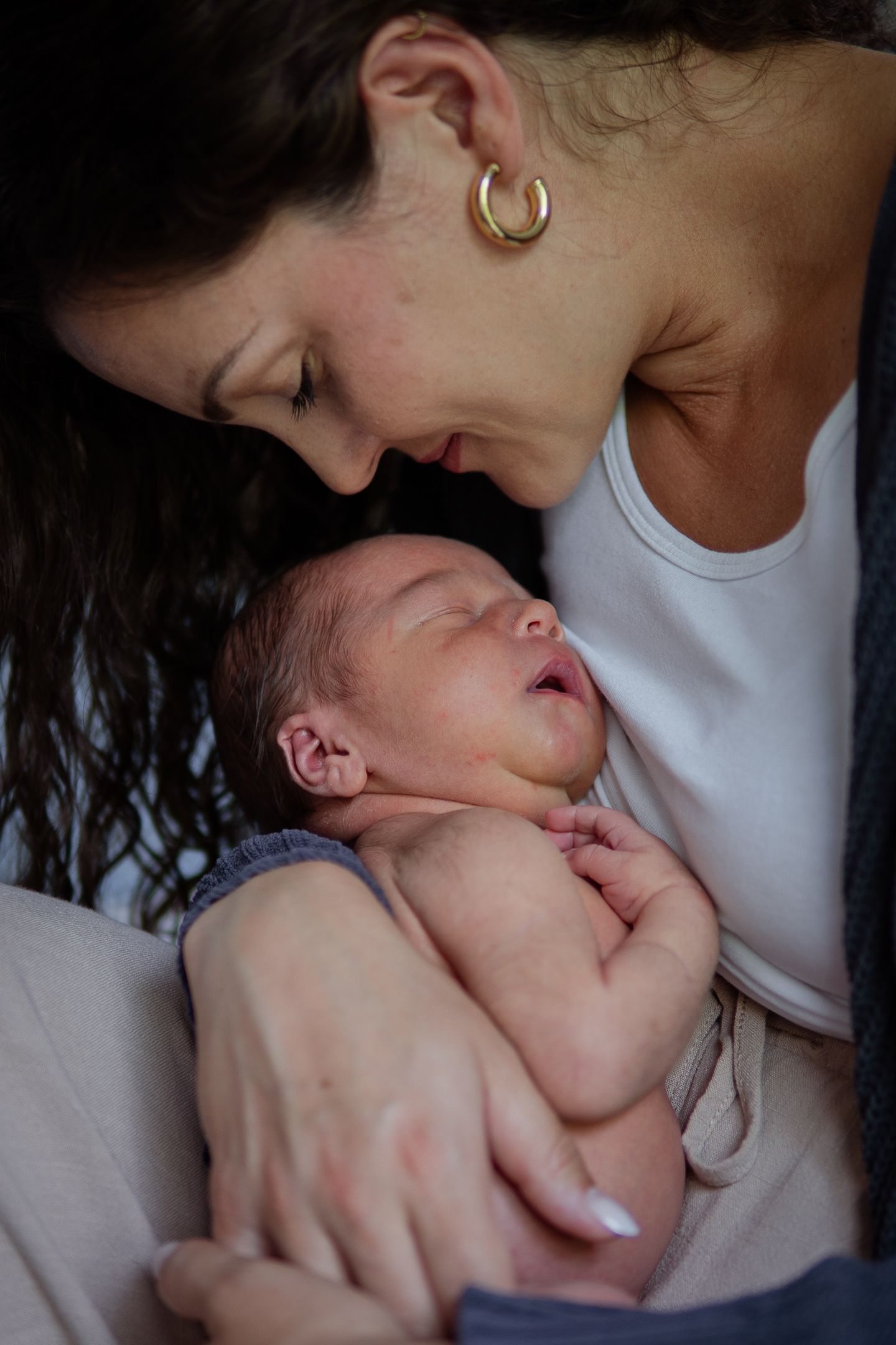 A mother holds and gazes lovingly at her newborn baby in natural window light.
