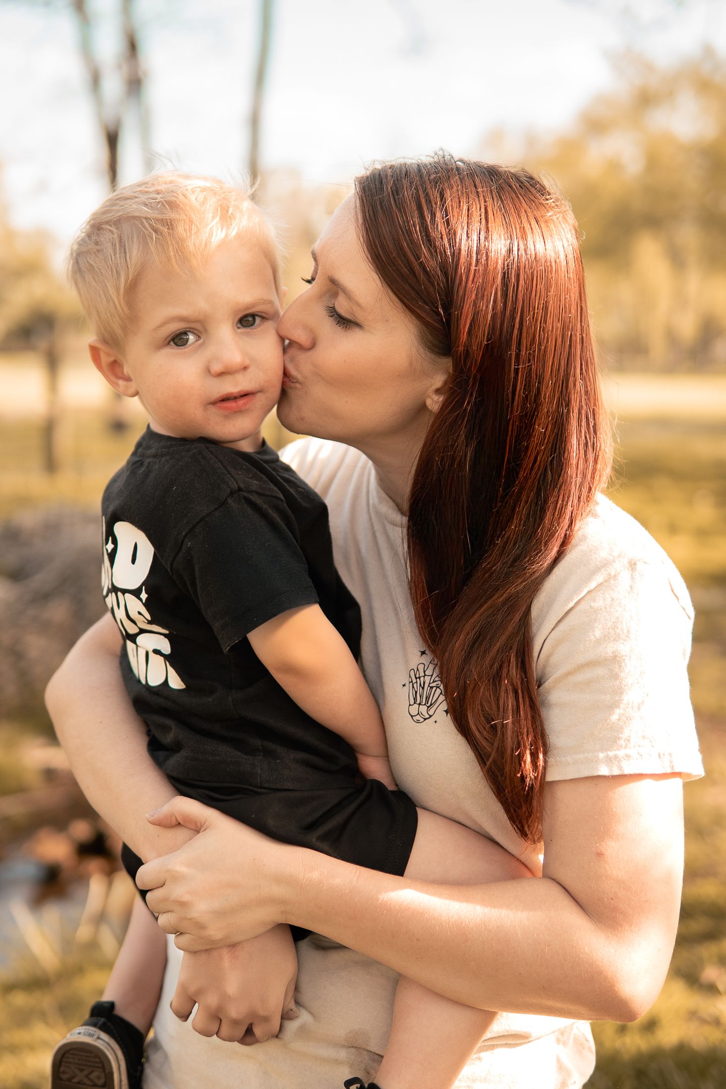 A tender outdoor portrait of parent and child sharing an affectionate moment in warm autumn lighting.