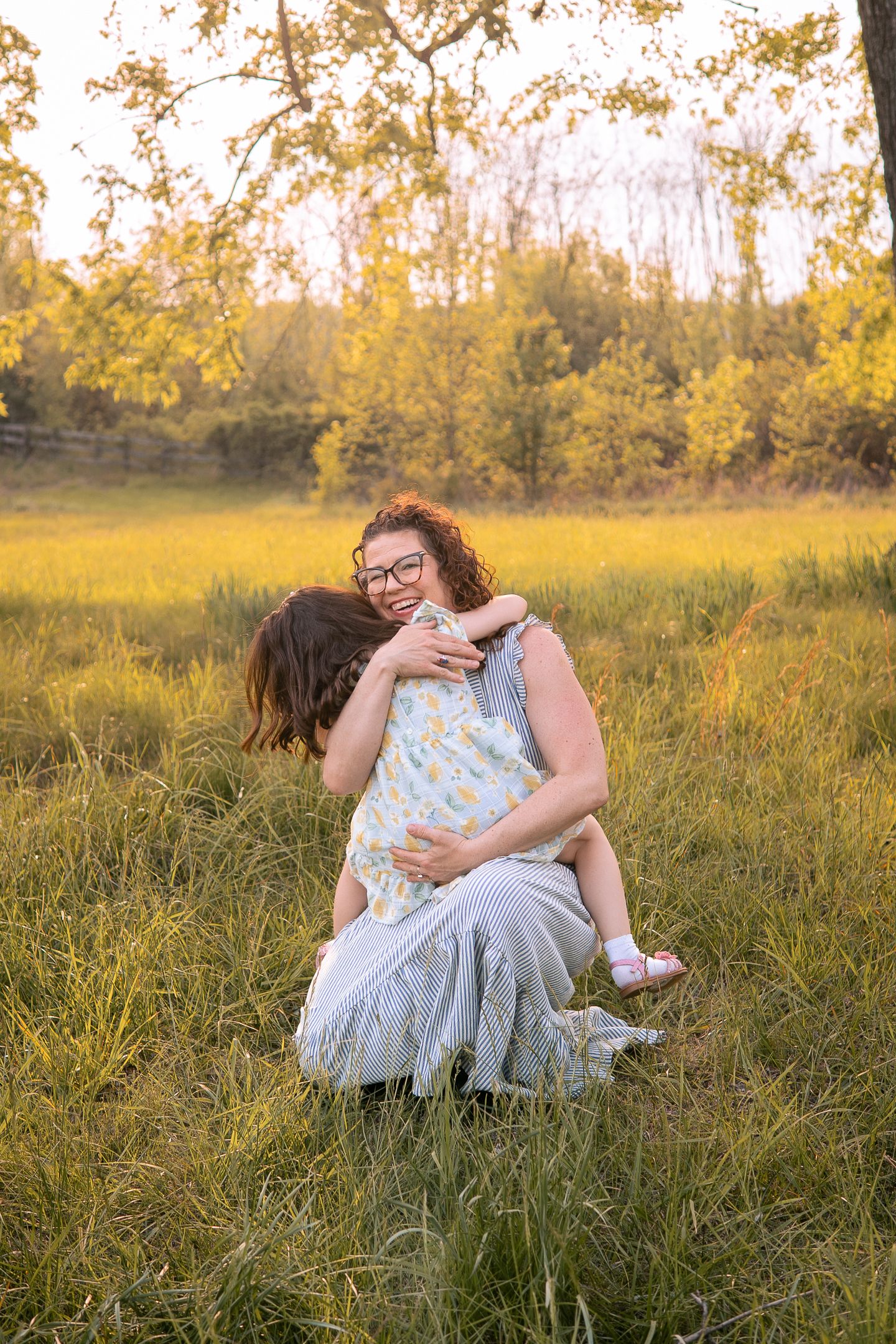 Tender embrace of parent and child during golden hour photography session in a sunlit meadow with autumn trees.