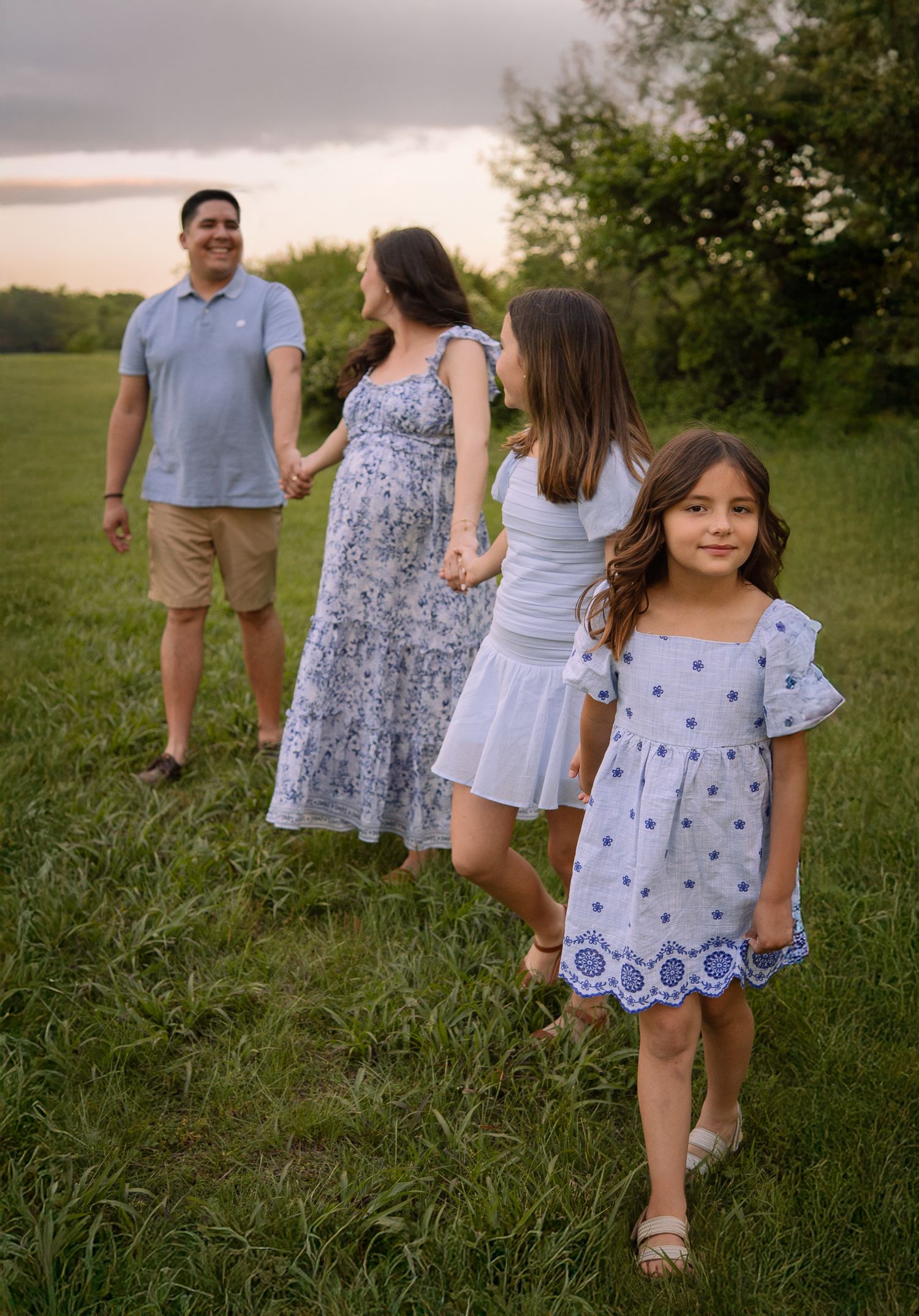 Family in coordinated outfits walking together through a grassy field at dusk.