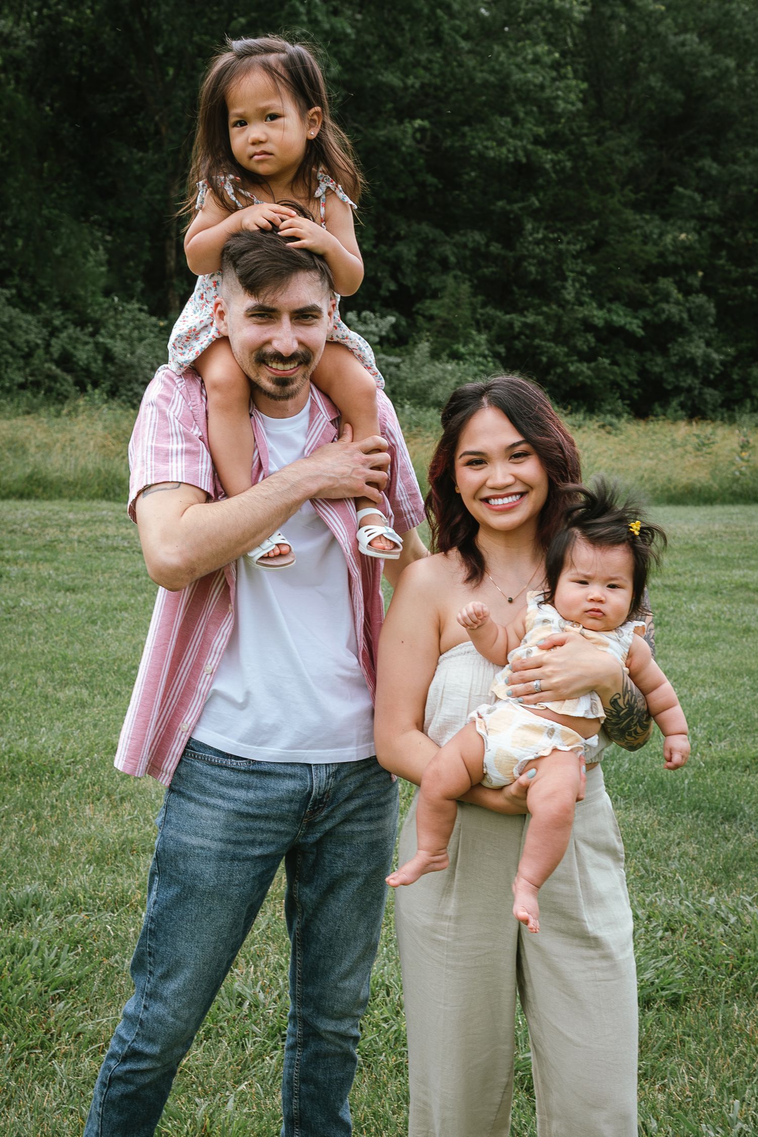 Playful outdoor family photoshoot with pink and beige outfits in a park setting.