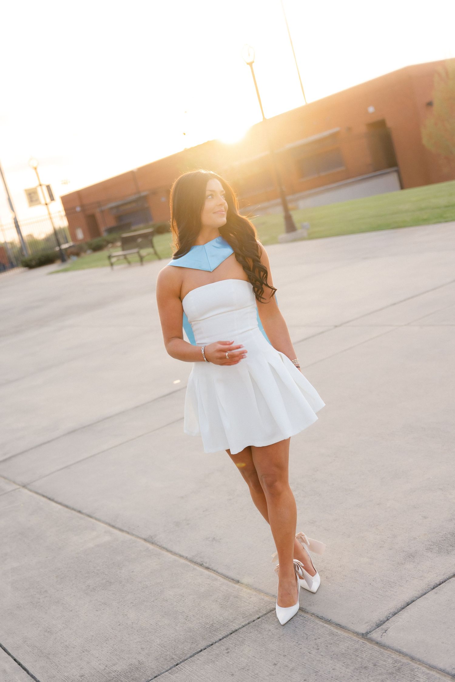 Young woman in white strapless dress with blue collar posing outdoors at golden hour sunset.