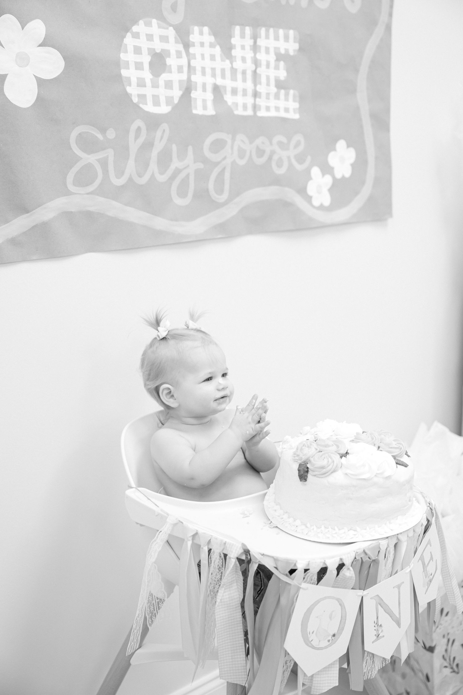A black and white photo shows a baby in a high chair reaching for their first birthday cake.