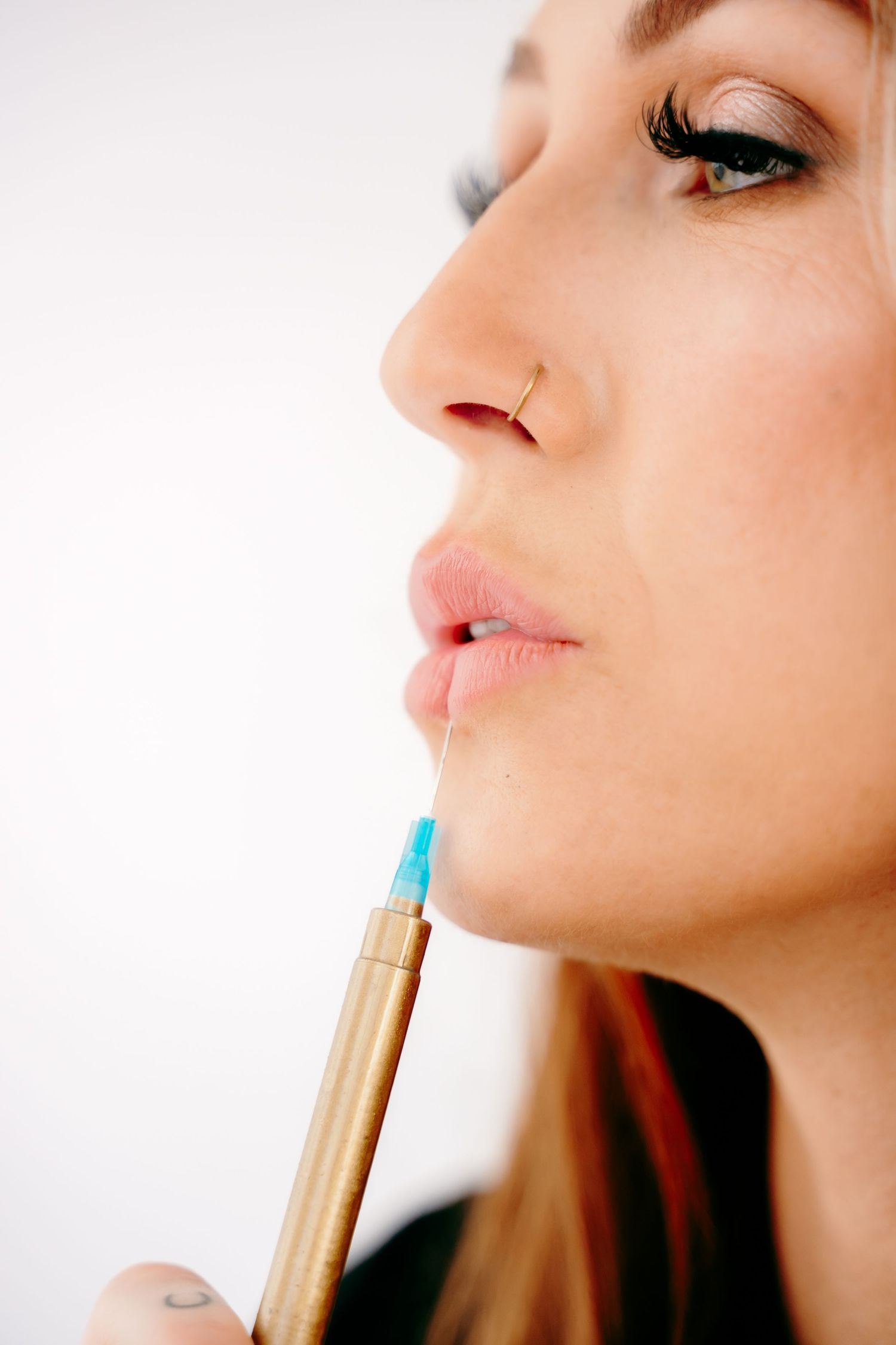 Close up of a person applying lip gloss with a gold applicator wand in soft lighting.