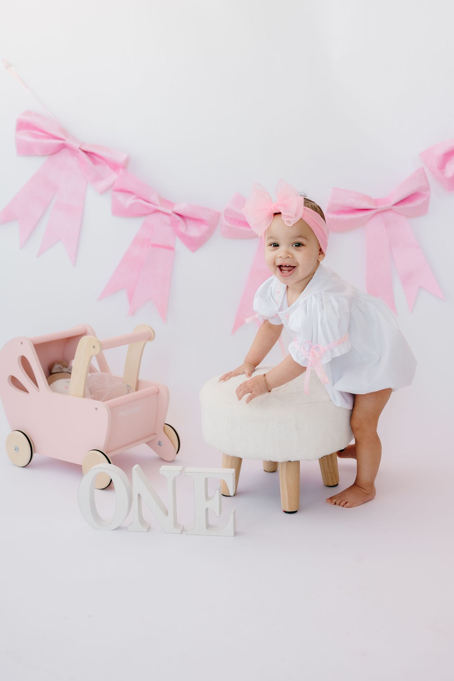 Pink and white themed baby photoshoot setup with decorative bows and letters.