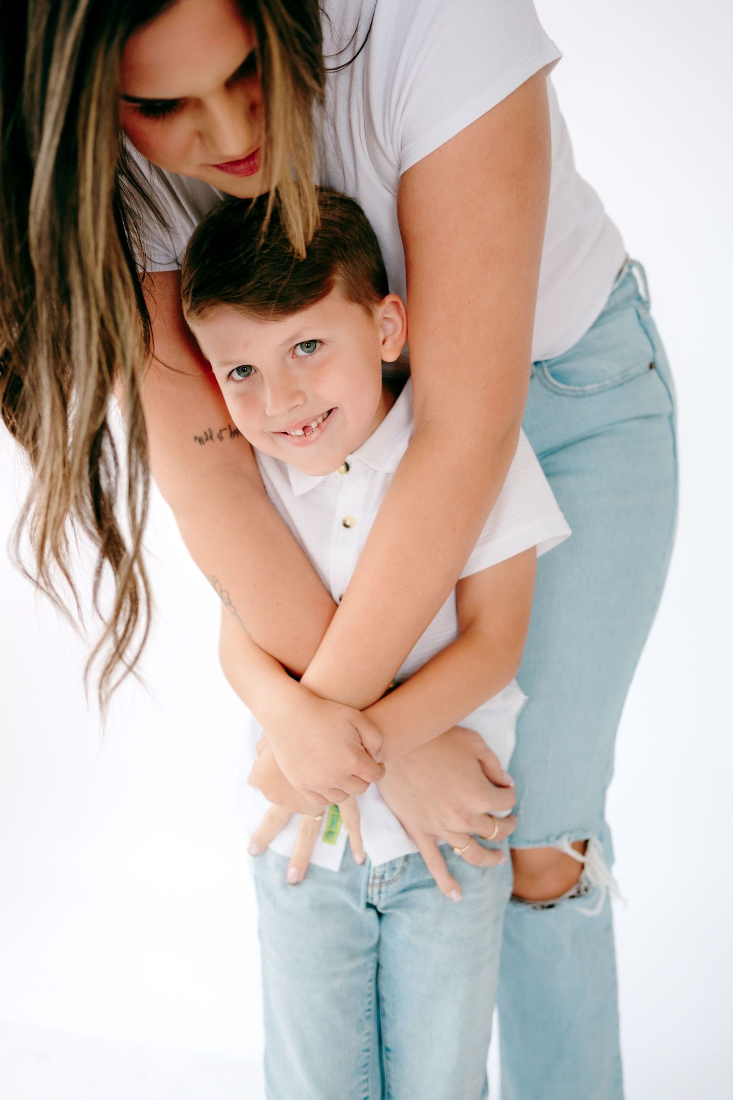 Parent and child share tender embraces in matching light blue and white outfits against white background.
