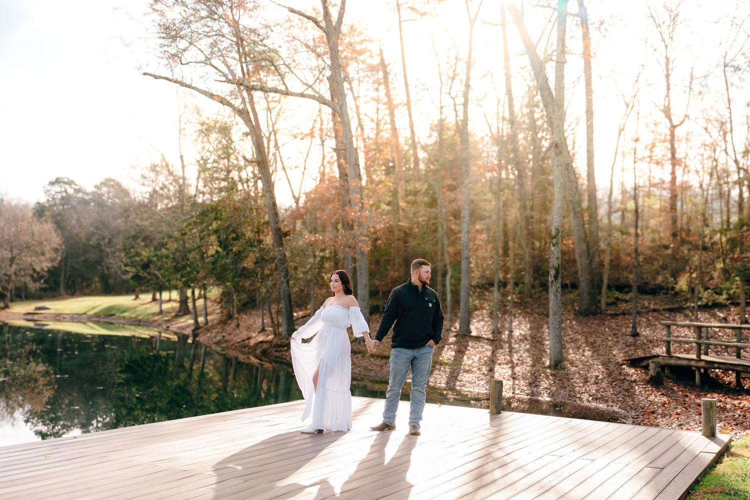 Couple walks along wooden dock over calm lake surrounded by winter trees.