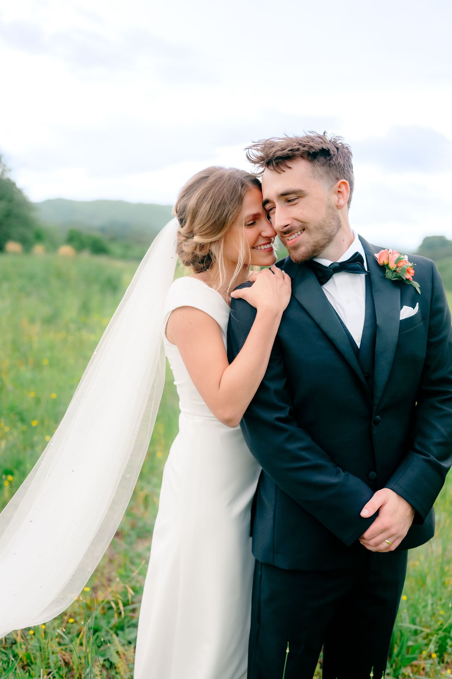 Happy couple shares joyful moment in sunny meadow during wedding portraits.