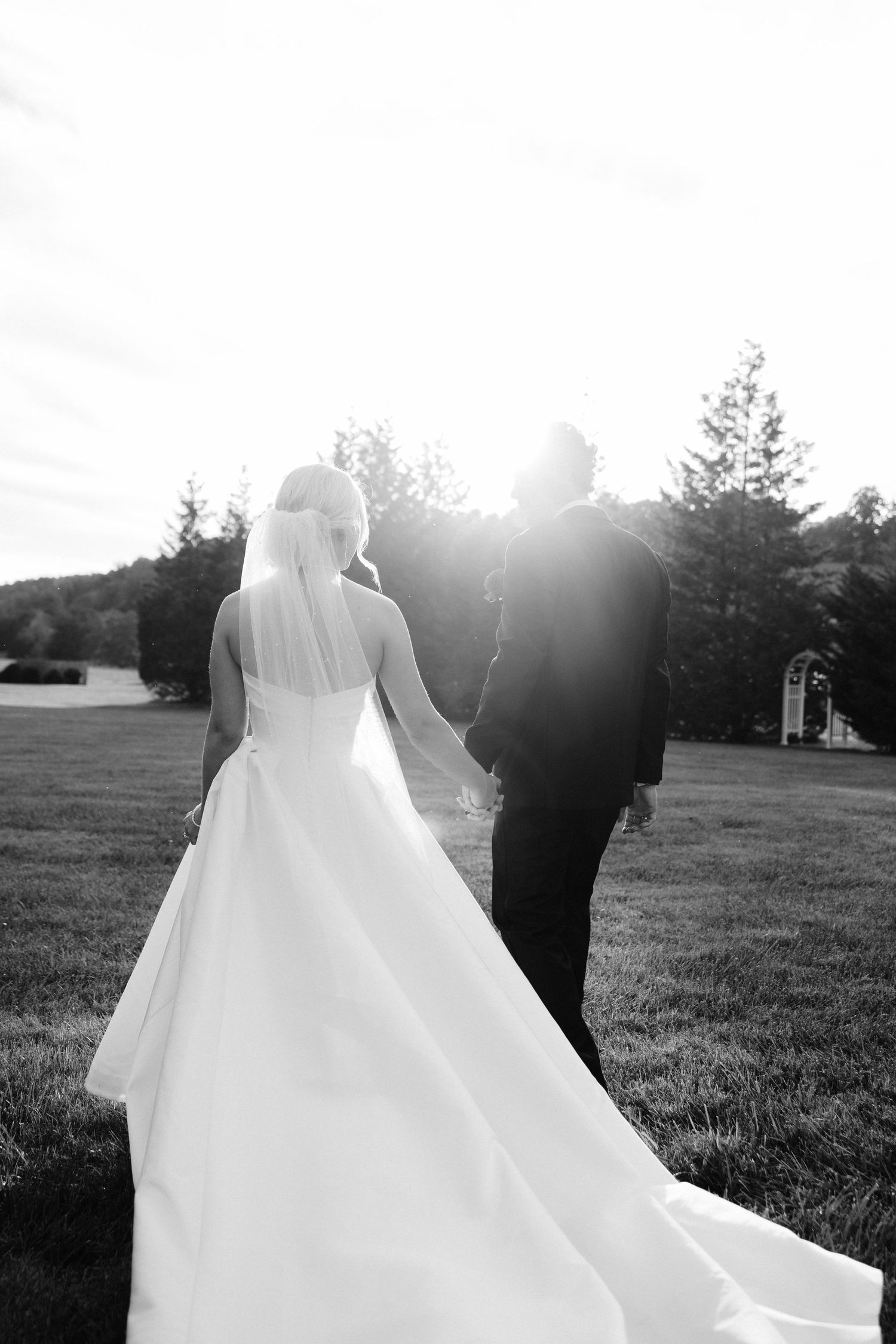 Silhouetted wedding couple walks through field at golden hour.