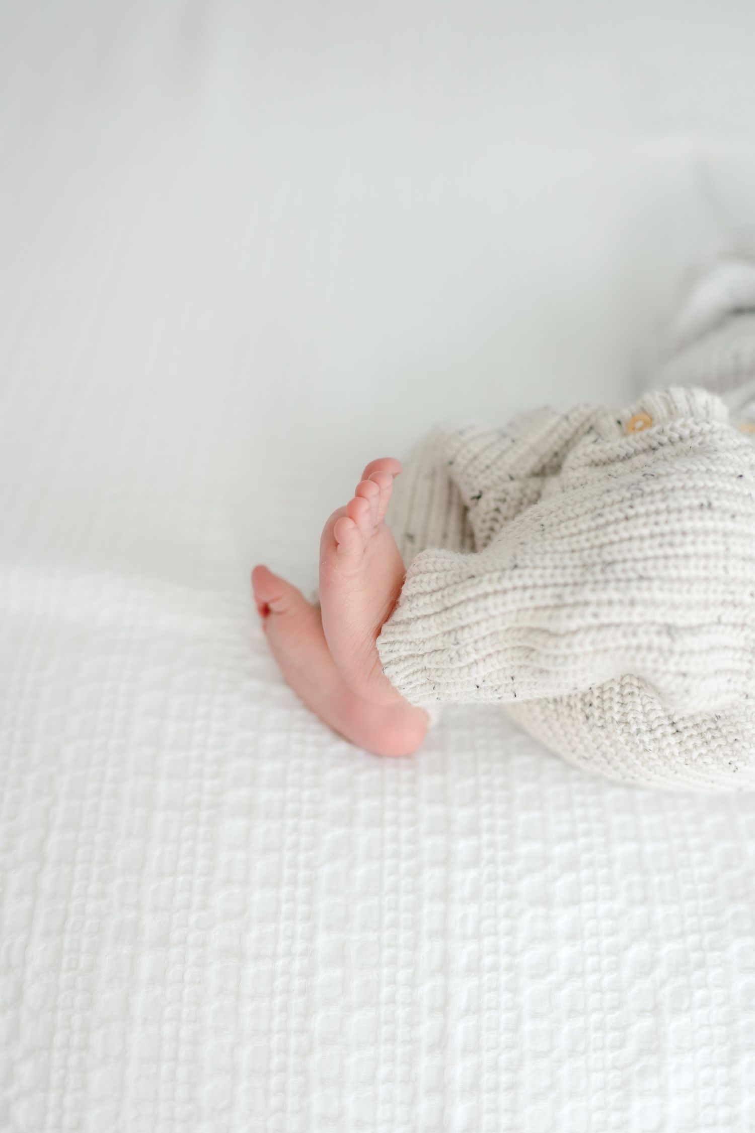 Tiny baby feet peek out from beneath a cozy white knit blanket.