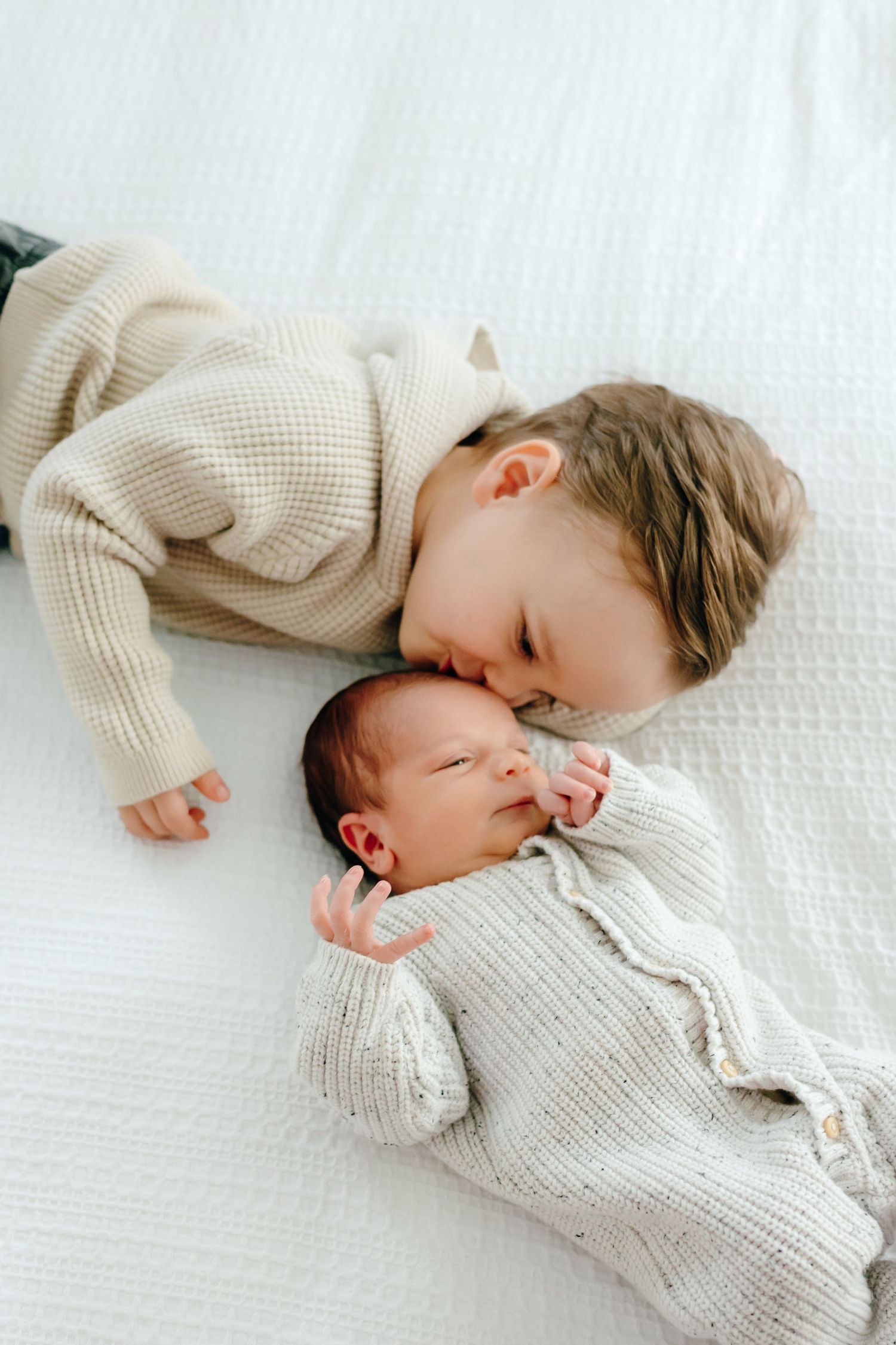 Two people in cream colored sweaters lying close together on white bedding.